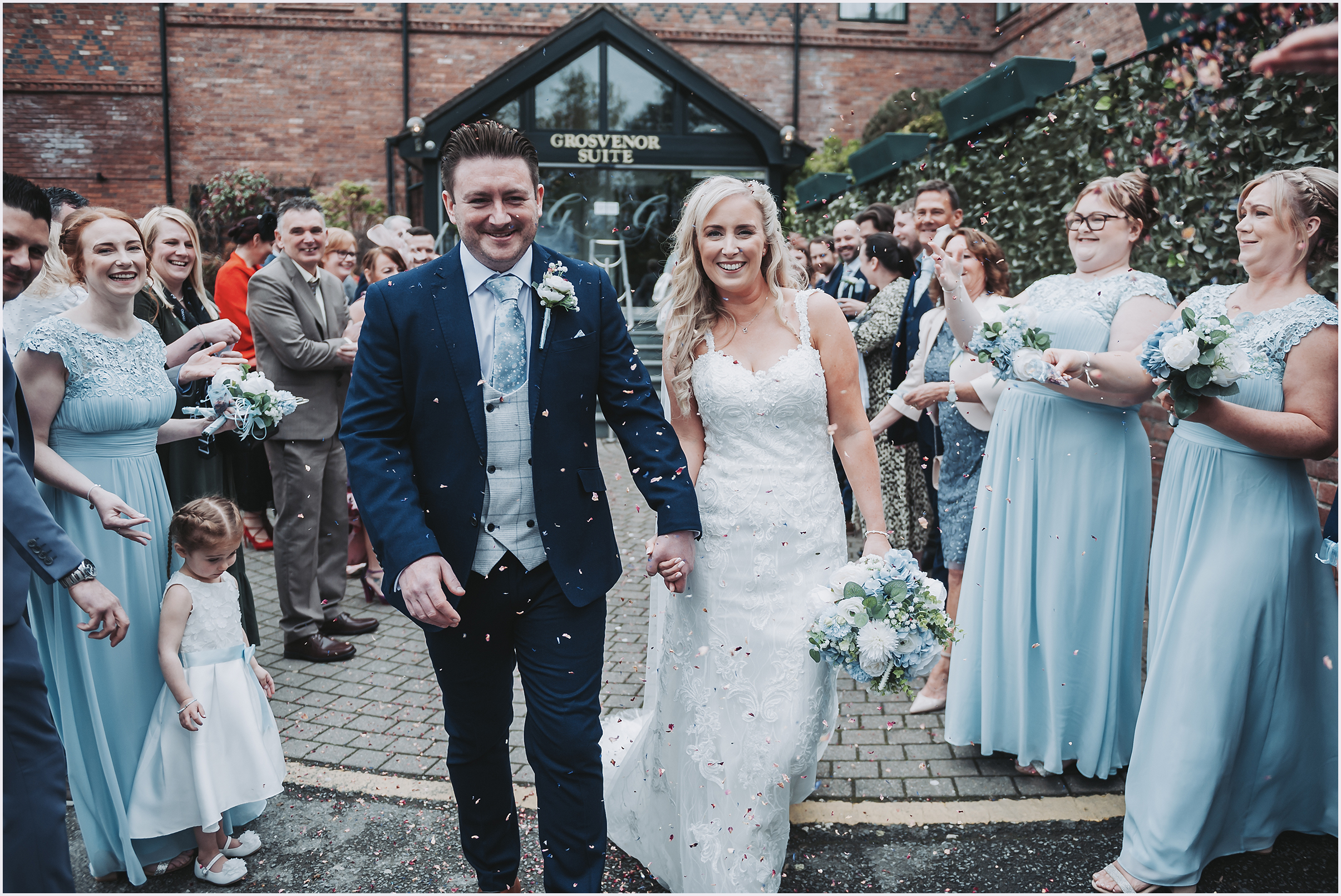 A newly married couple smile at the camera as their guests throw confetti at them at The Grosvenor Pulford Hotel and Spa