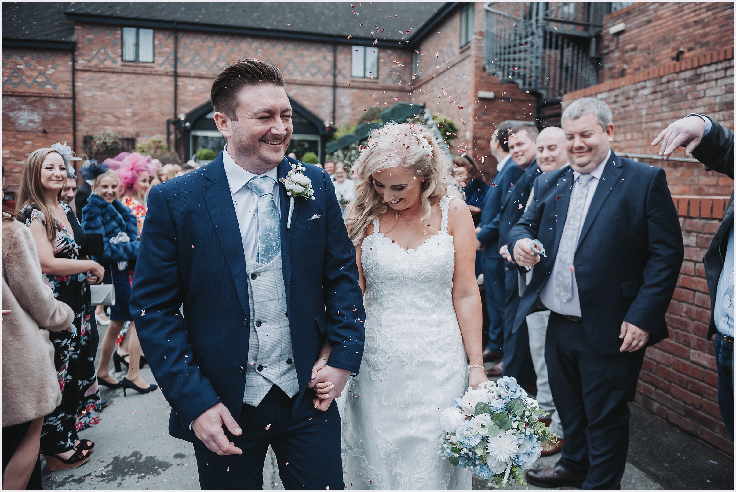 A newly married couple smile happily while confetti is thrown at them. Image captured by North Wales wedding Photographer Helena Jayne Photographer.