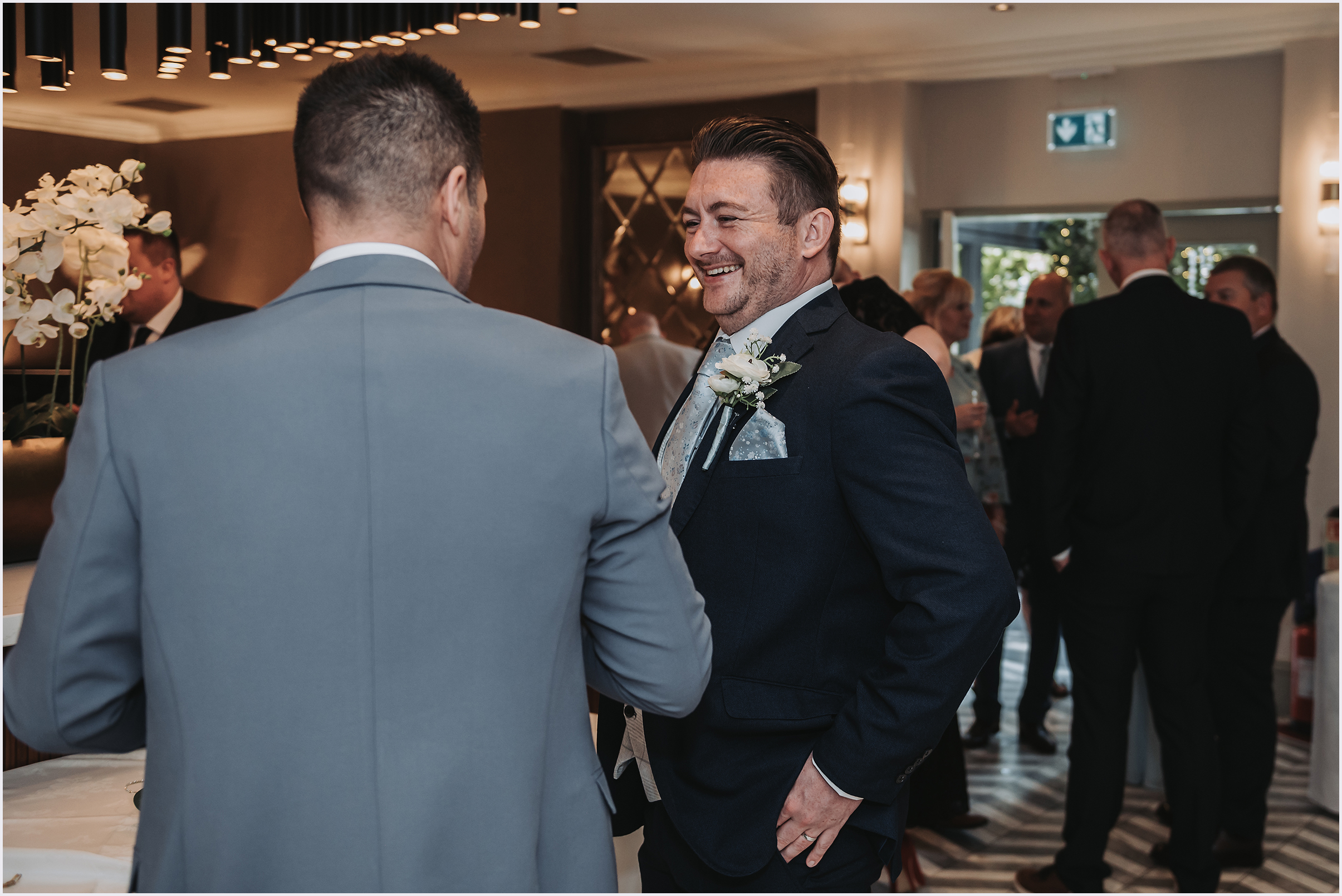 A groom chatting happily with one of his guests during the drinks reception at a wedding.