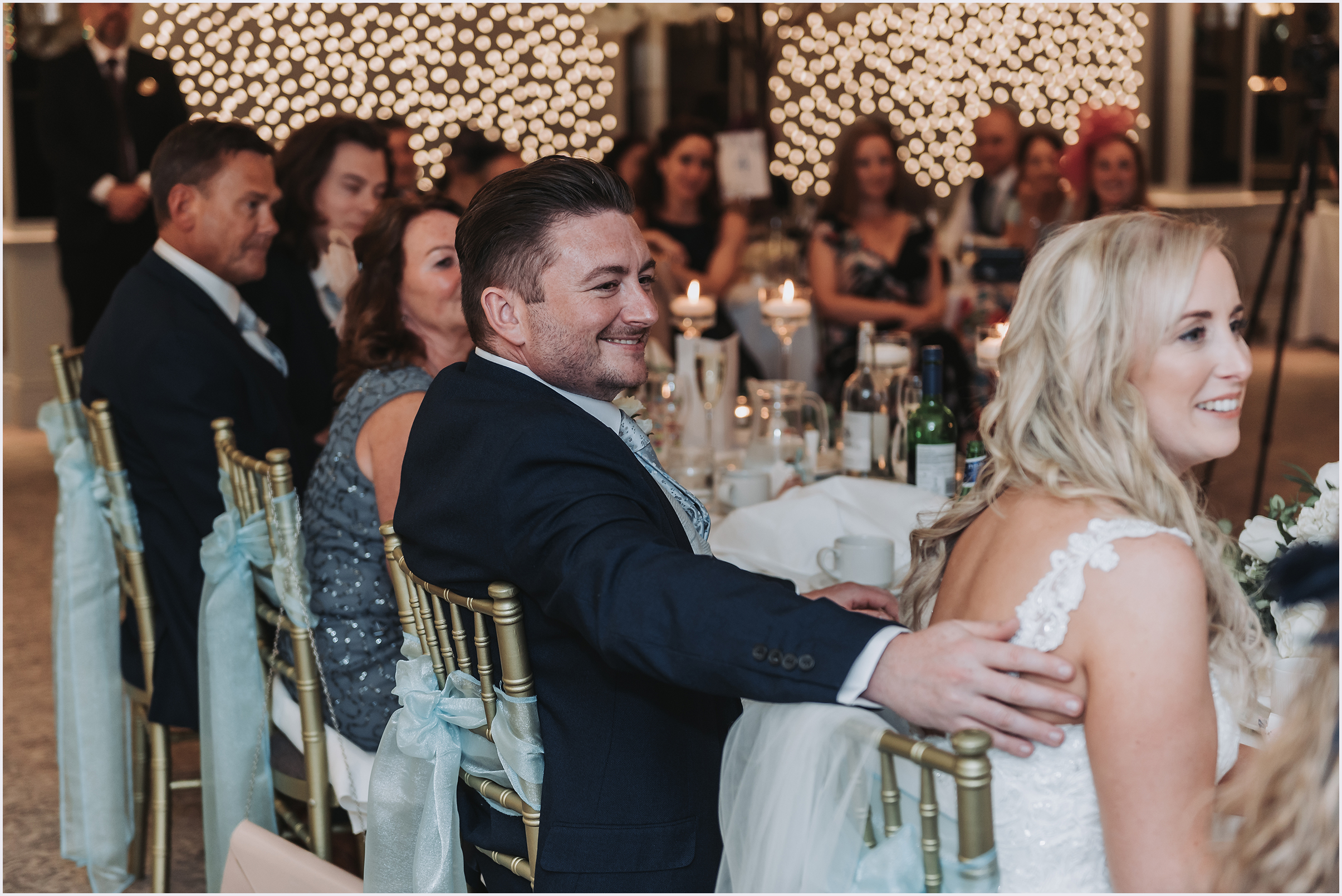 A bride smiles with his arm around his new bride's back as the speeches are said at The Grosvenor Pulford Hotel and Spa.