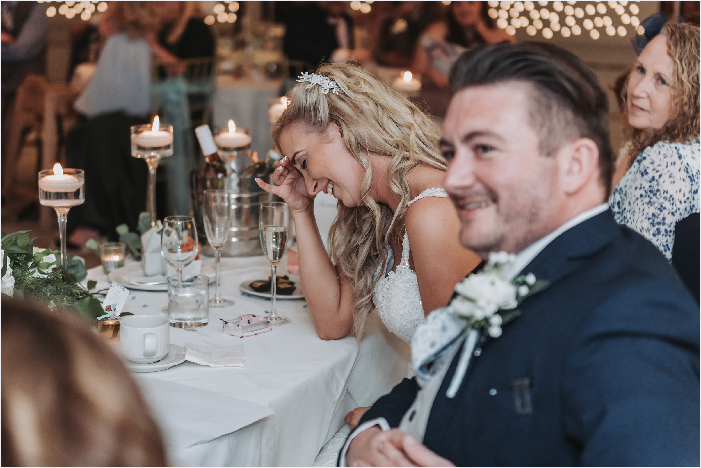 A bride holding her head in her hand laughing at the best man's speech.
