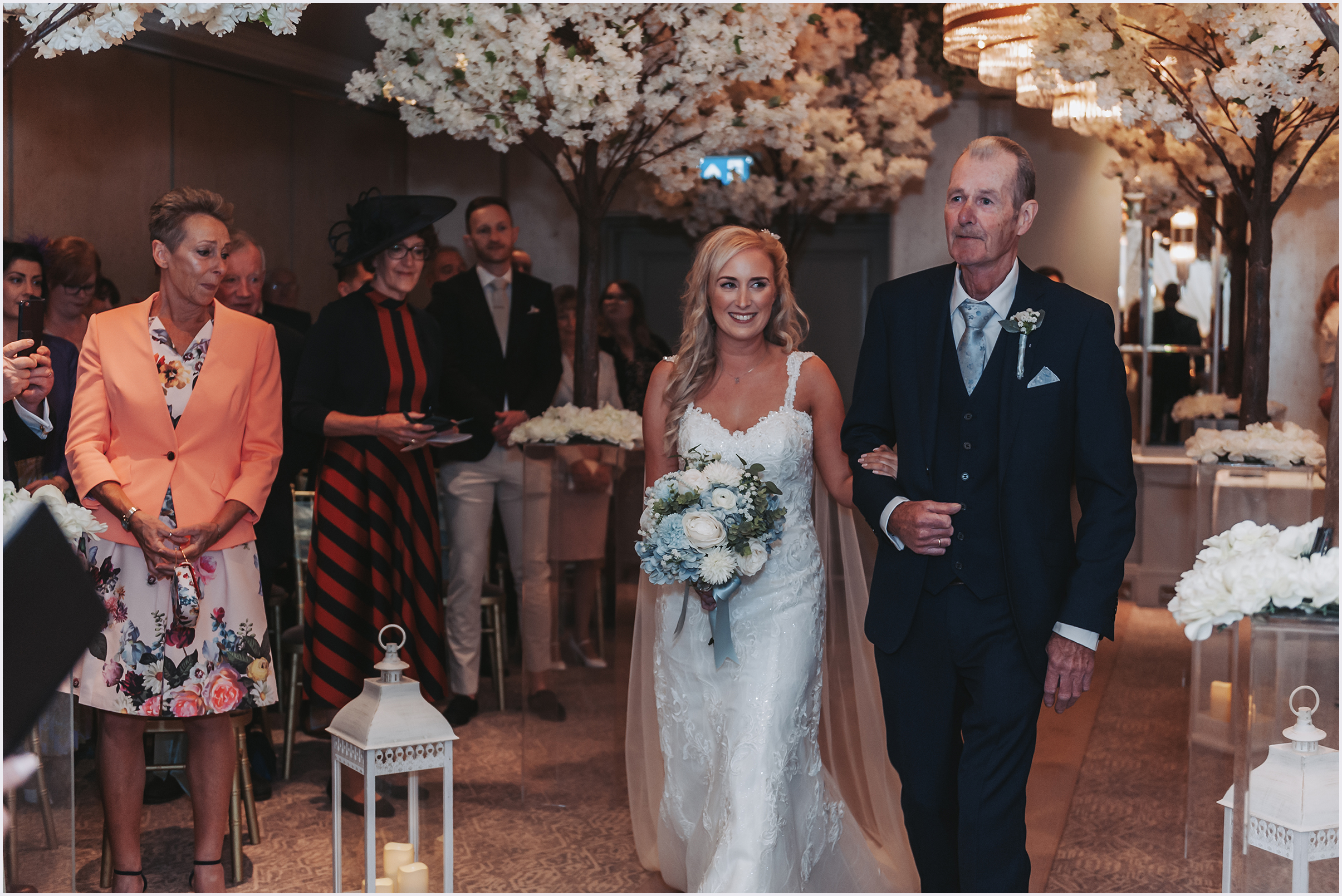A bride with her hand linking her father's arm walking down the aisle during her wedding ceremony at The Grosvenor Pulford Hotel and Spa