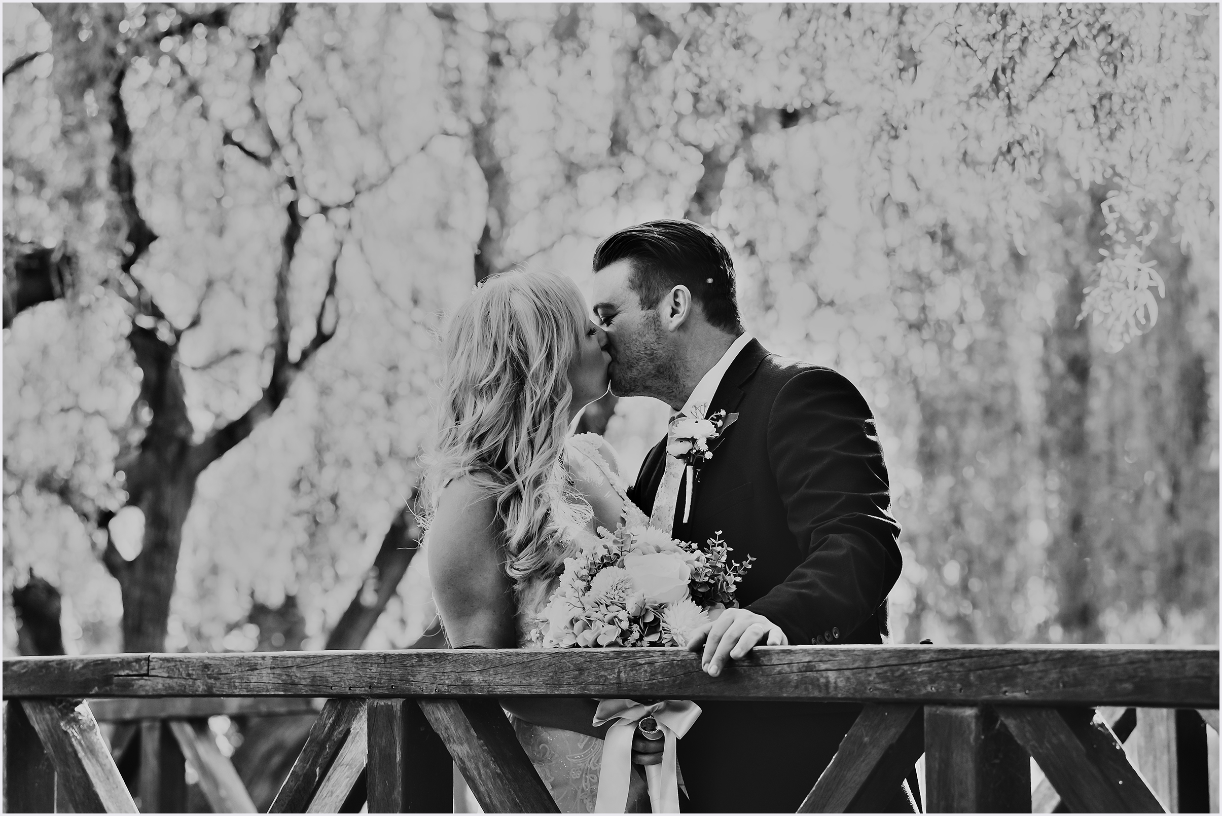 A groom rests his hand on the railing of a wooden bridge as he and his new wife share a kiss during their bride and groom photo shoot at The Grosvenor Pulford Hotel and Spa.
