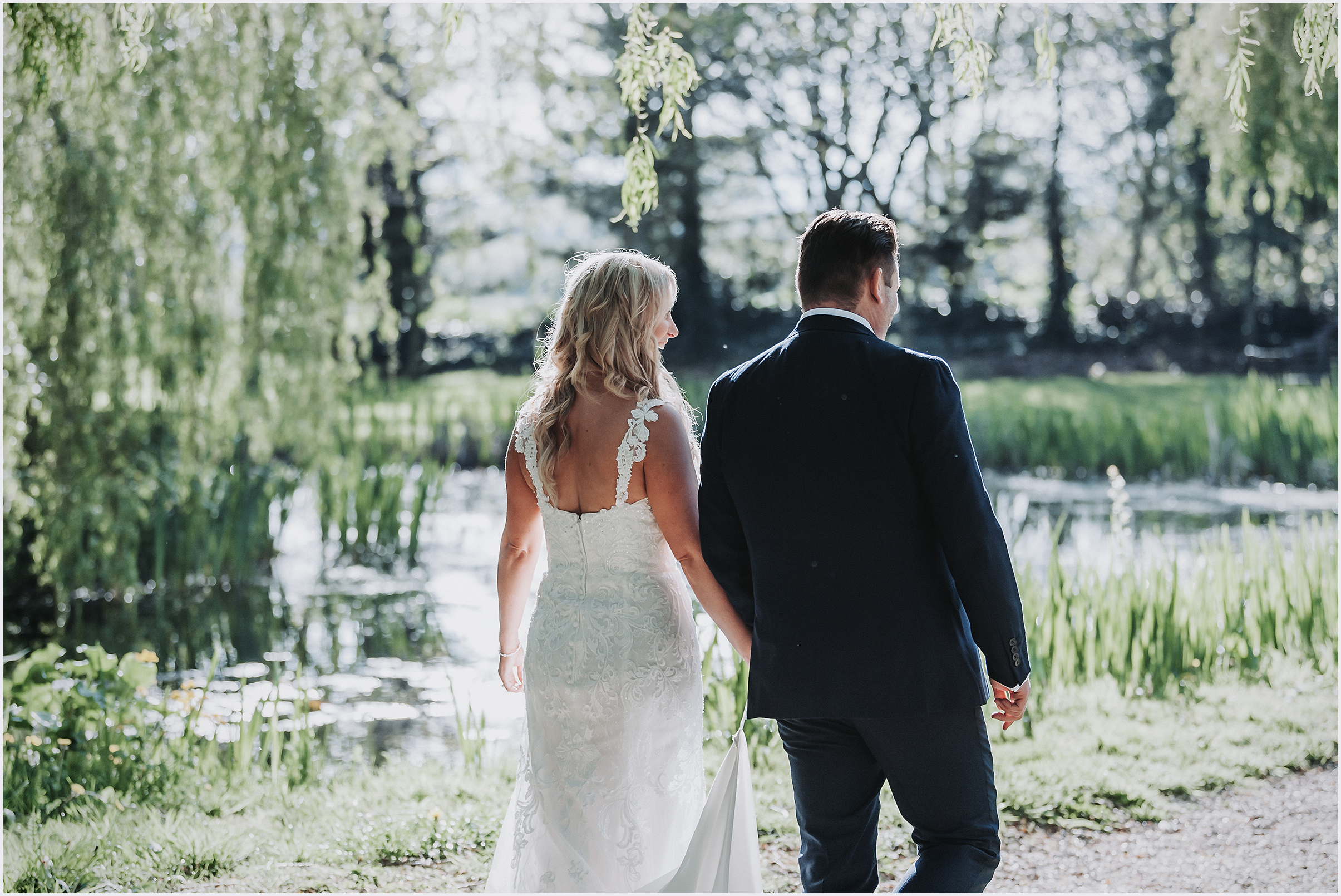 A bride and groom walking hand in hand by a lake at The Grosvenor Pulford Hotel and Spa