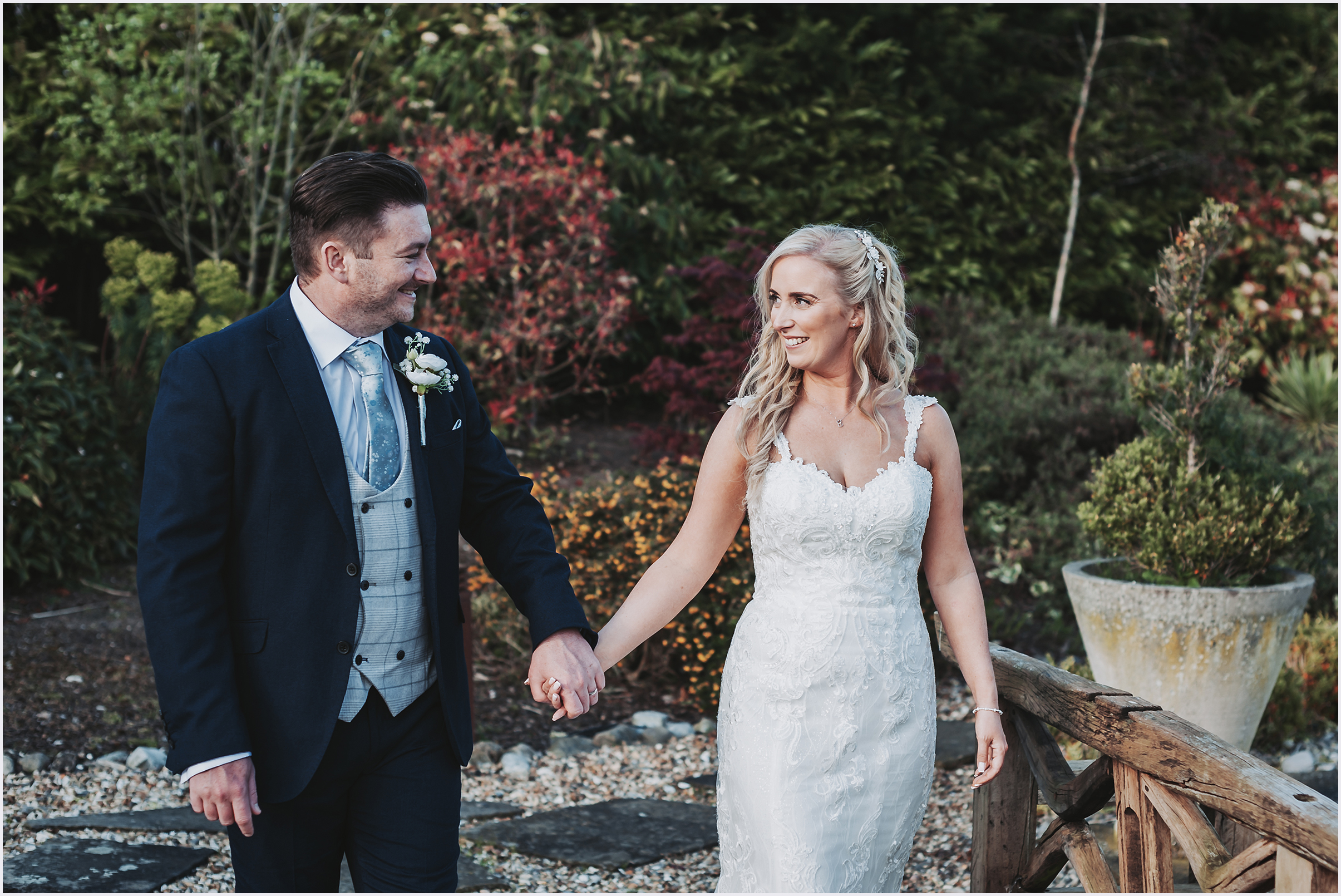 A bride and groom walk hand in hand smiling at each other during their couples photographs.  Image captured by Cheshire wedding photographer Helena Jayne Photography