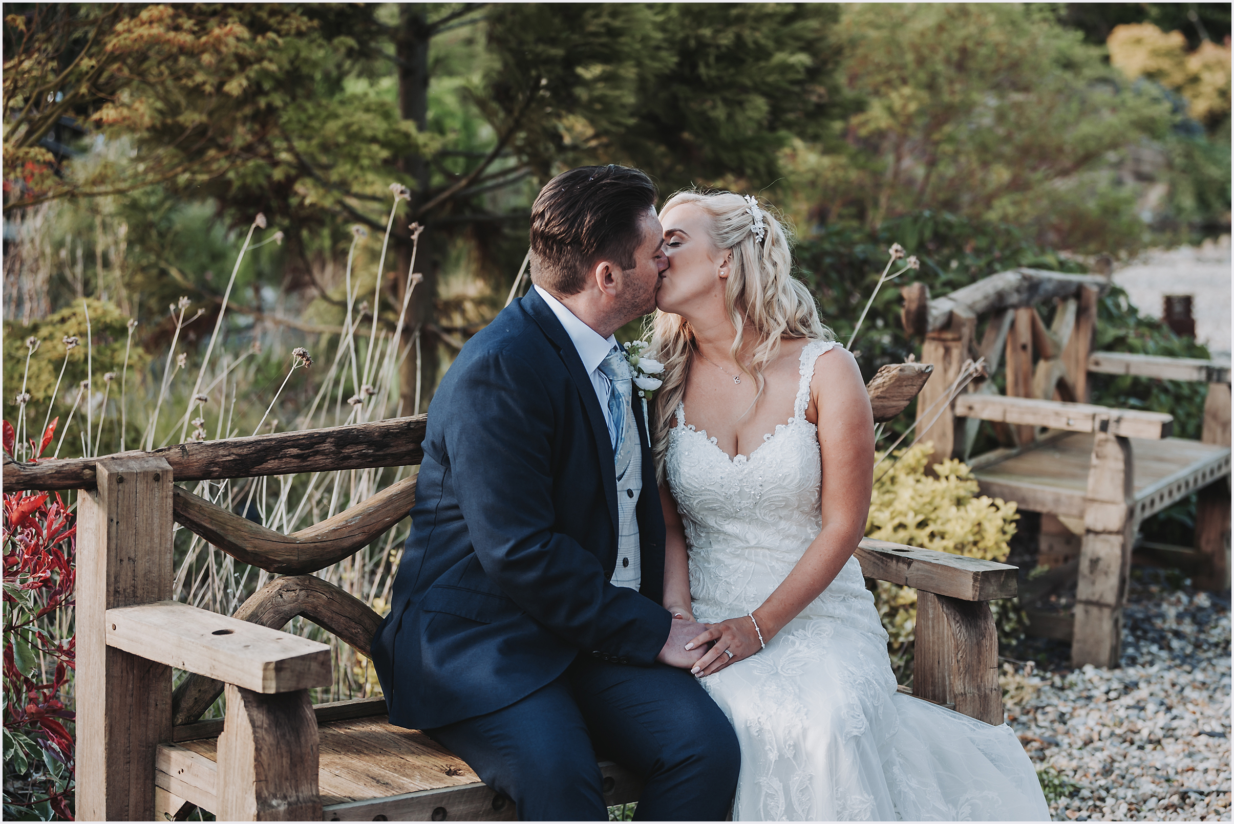 A newly married couple sitting on a beautiful wooden bench sharing a kiss in the Japanese Gardens at The Grosvenor Pulford Hotel and Spa.