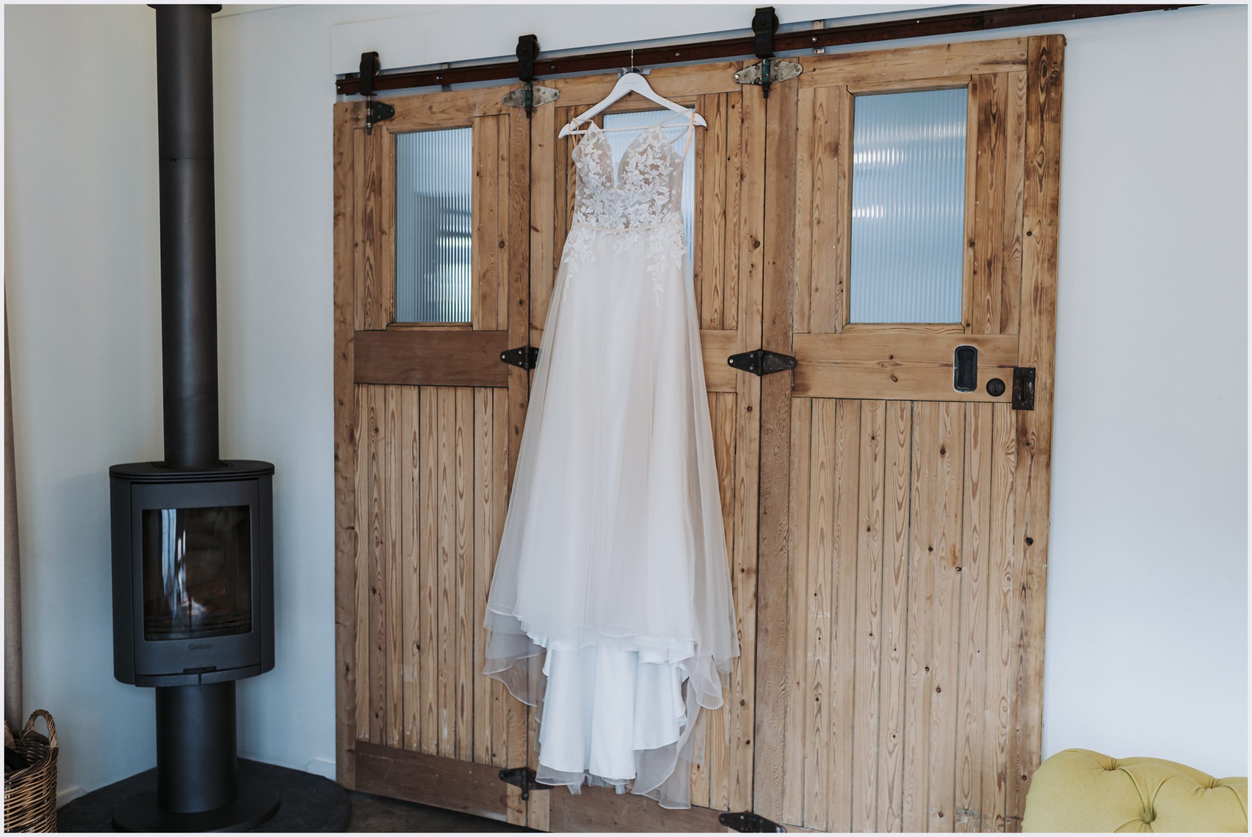 Bride's stunning lace wedding dress with a long train hanging on the rustic stable doors of a converted barn taken by north Wales wedding photographer Helena Jayne Photography