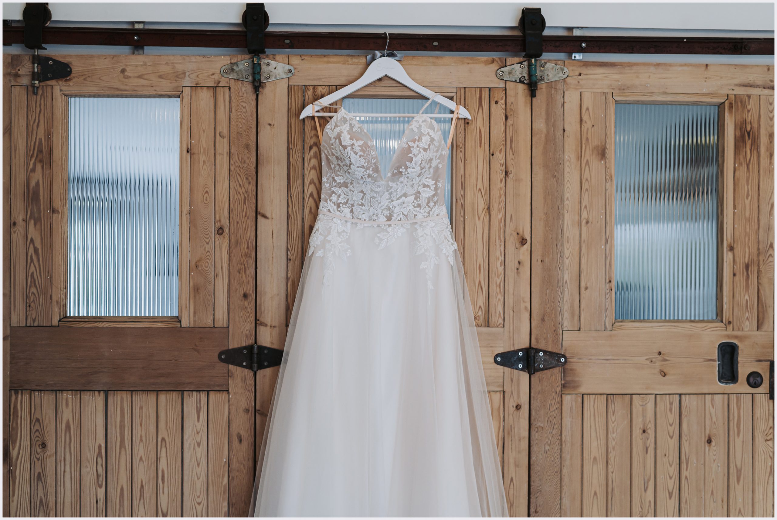 Bride's stunning lace wedding dress with a long train hanging on the rustic stable doors of a converted barn taken by Cheshire wedding photographer Helena Jayne Photography