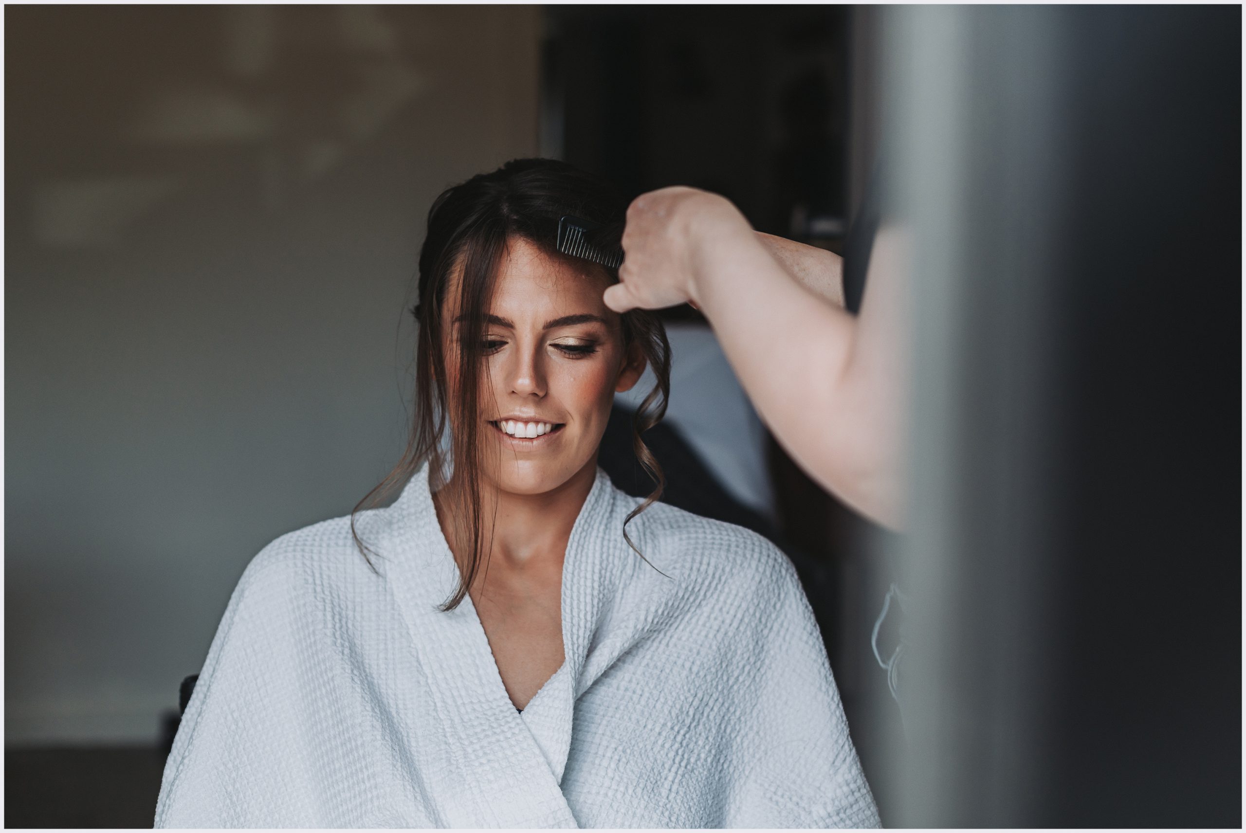 A beautiful bride wearing a white bath robe getting her hair done on the morning of her wedding.  Image captured by Helena Jayne Photography Cheshire wedding photographer