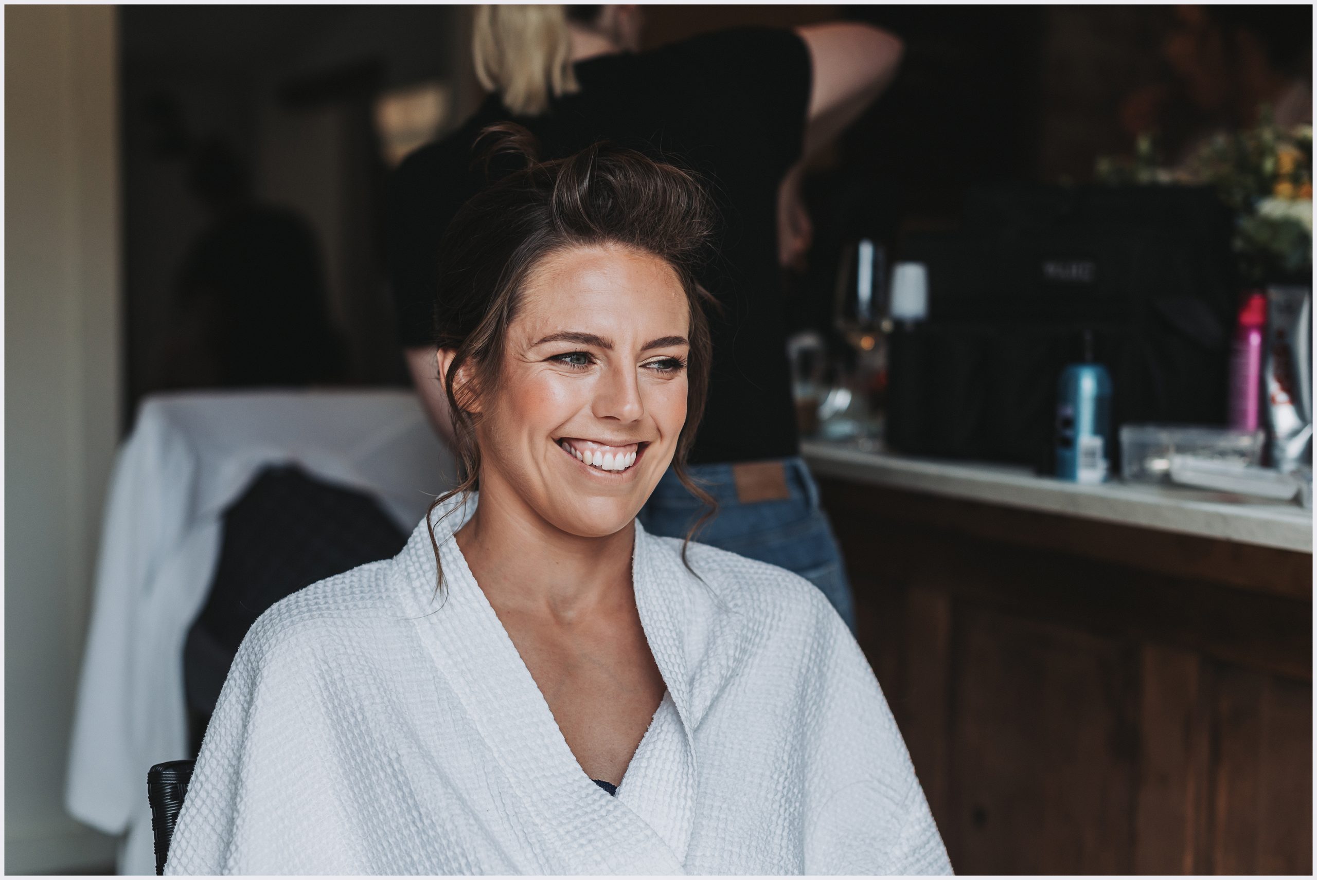 A beautiful smiling bride to be wearing a white bath robe on the morning of her wedding.  Image captured by Helena Jayne Photography North Wales wedding photographer