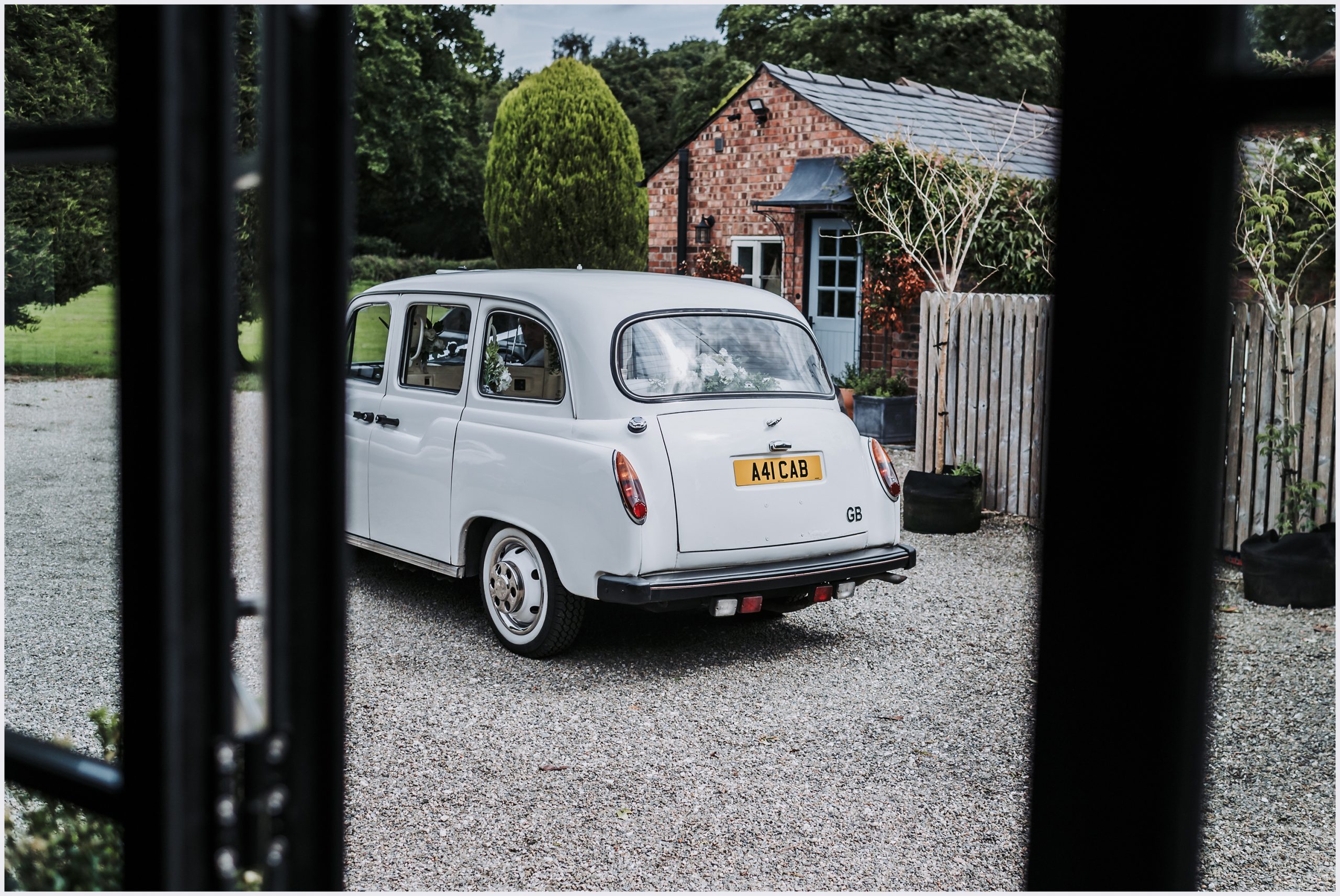 An old fashioned white cab parked on a gravel driveway.  Images taken by North Wales wedding photographer Helena Jayne Photography