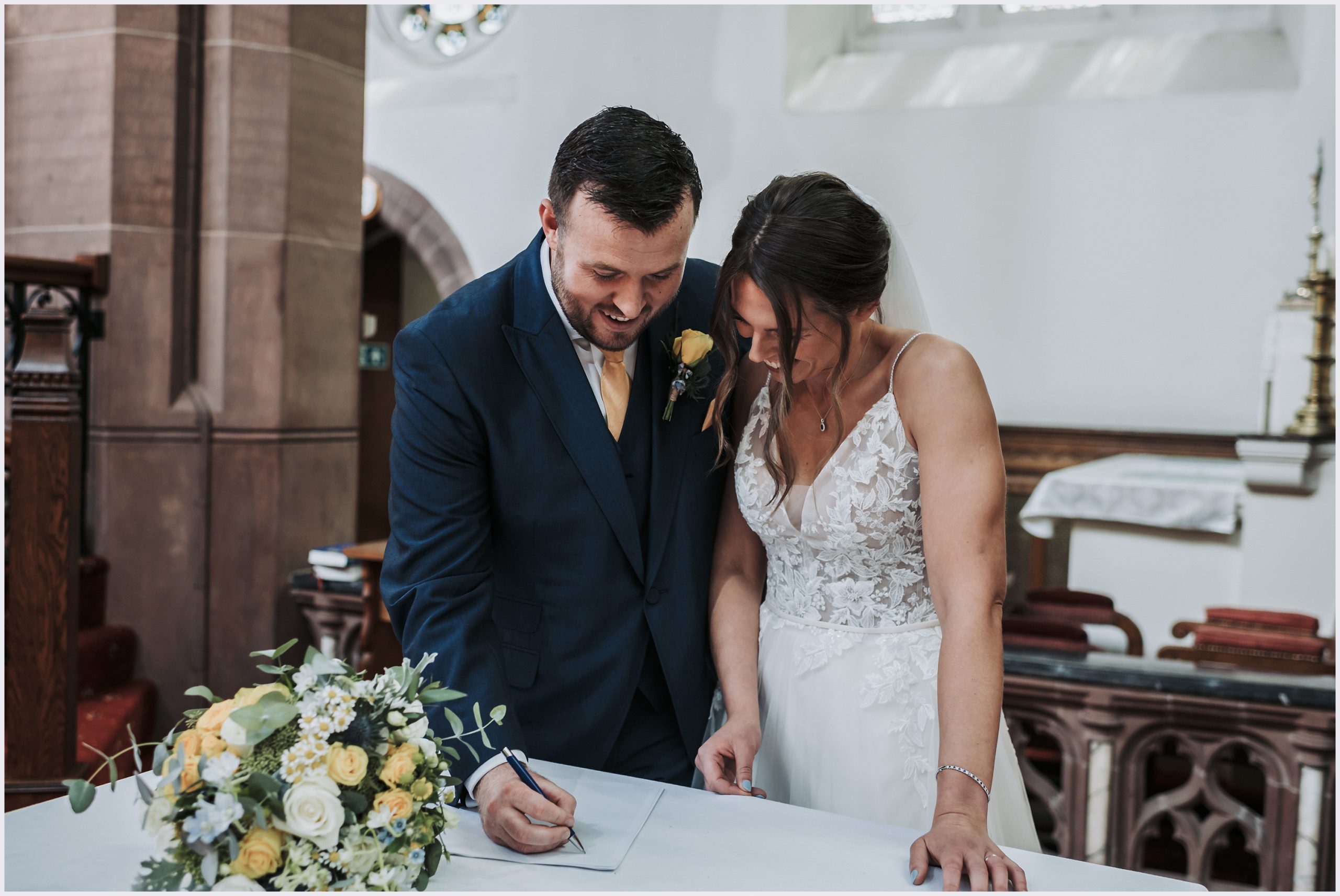A bride and groom look down smiling the register as they sign after their church wedding ceremony in Chester