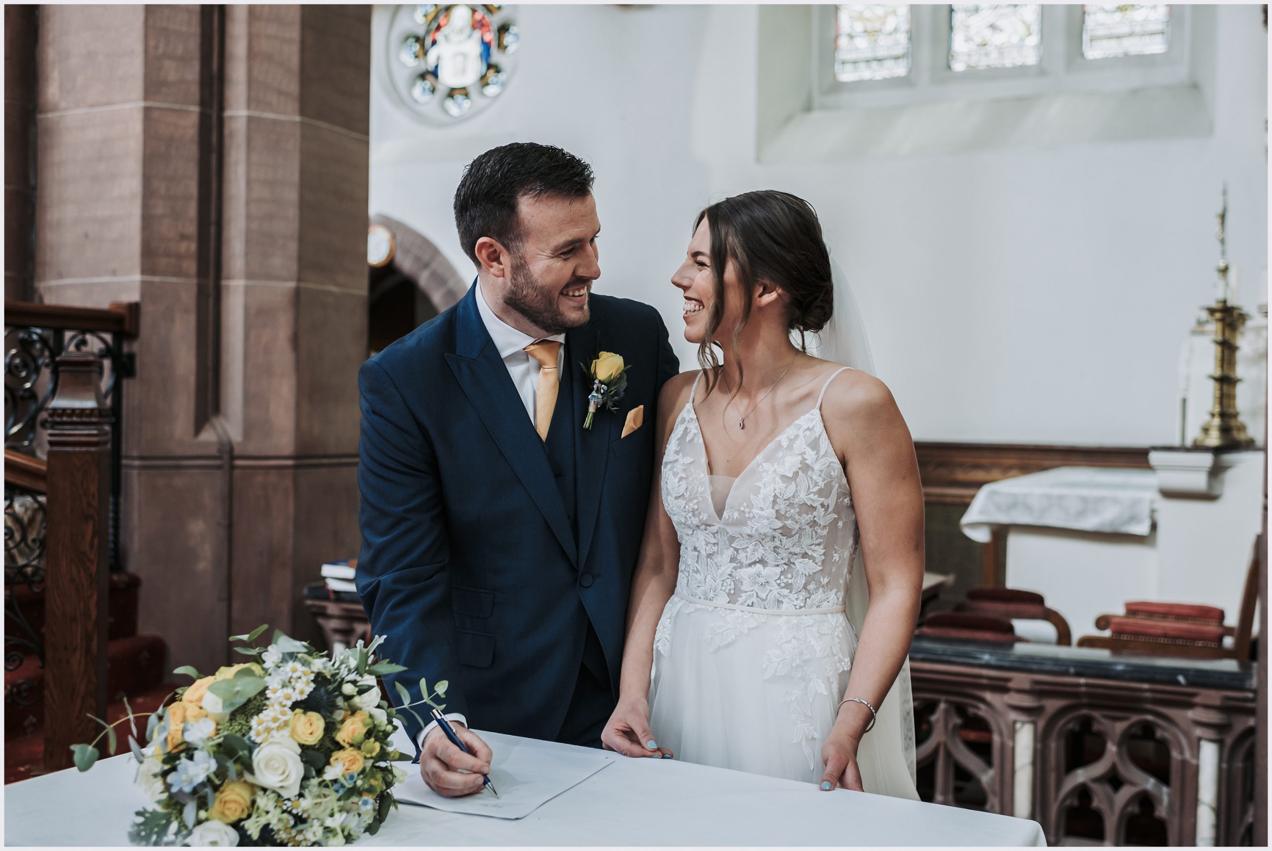 A bride and groom smile at each other after signing the register in a church in Chester