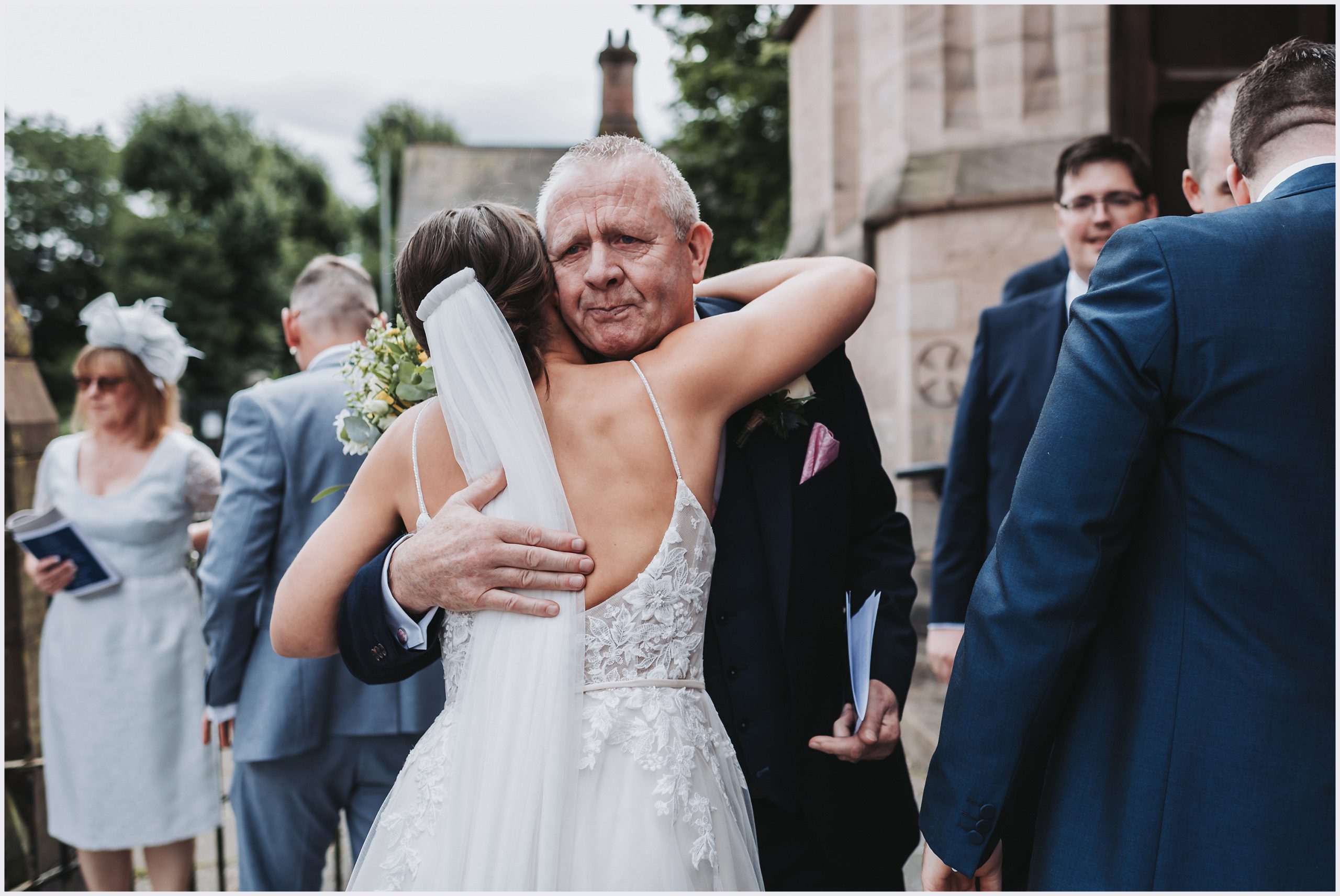 A guest emotionally hugs the bride after leaving the church.  Image captured by Cheshire wedding photographer Helena Jayne Photography