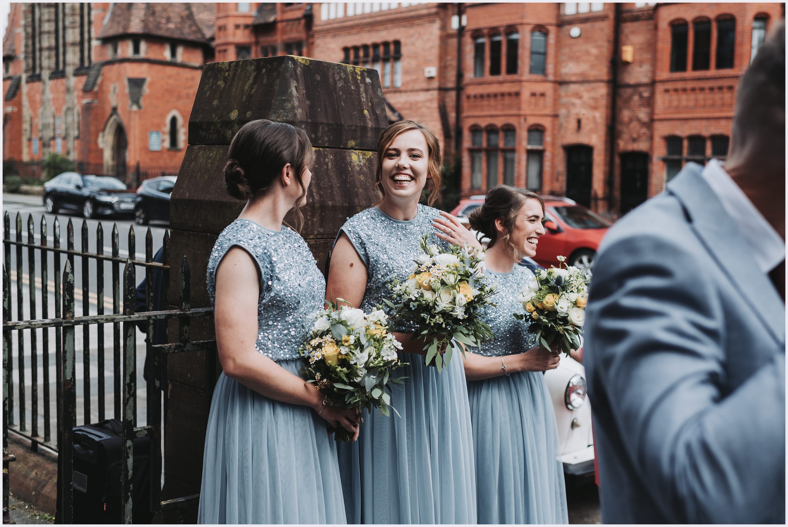 Three smiling bridesmaids stand together in their gorgeous pale blue dresses after the wedding ceremony of their best friends.  Image captured by Helena Jayne Photography a wedding photographer based in Chester