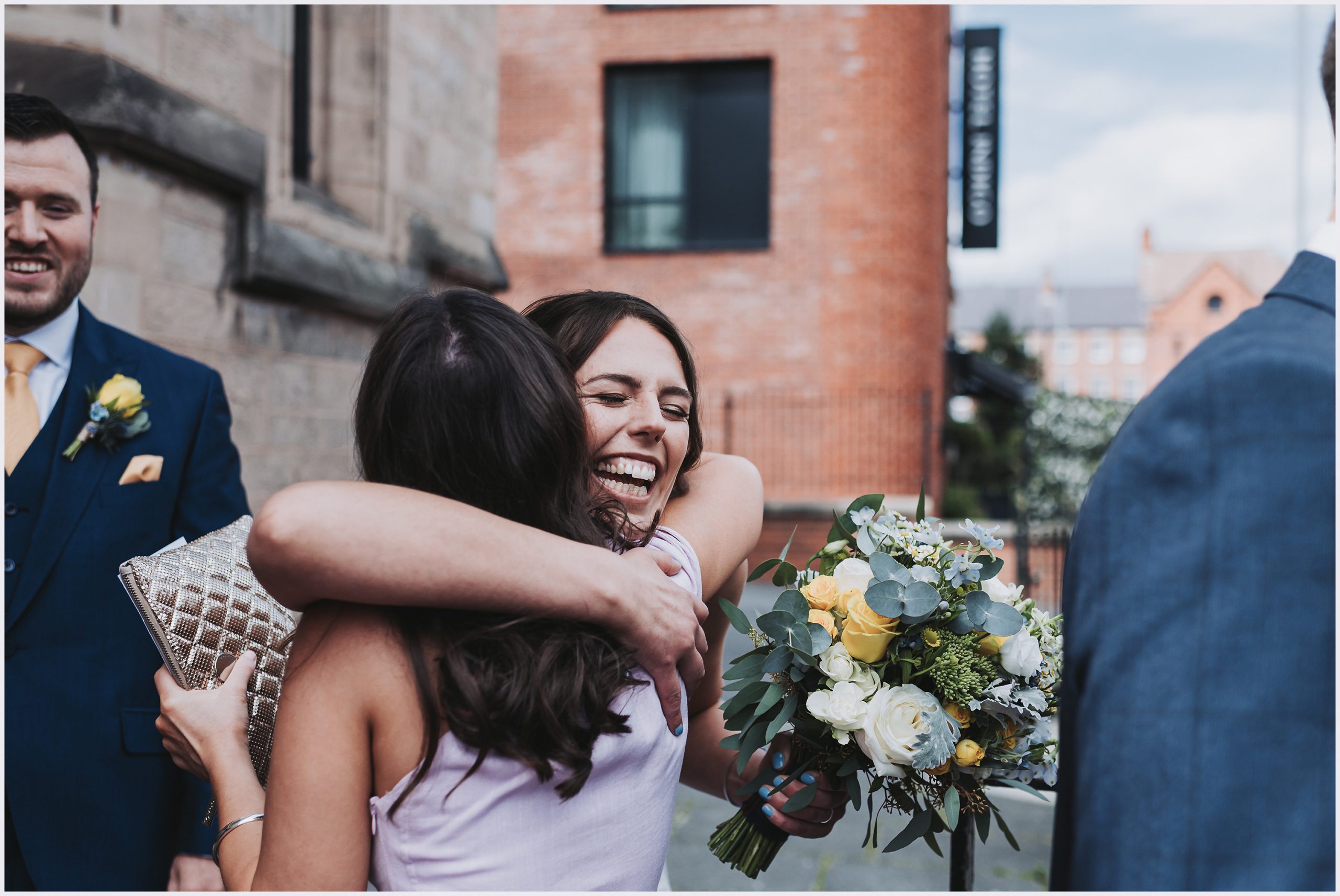 A smiling bride excitedly hugs her friend outside the church where she has just got married.  