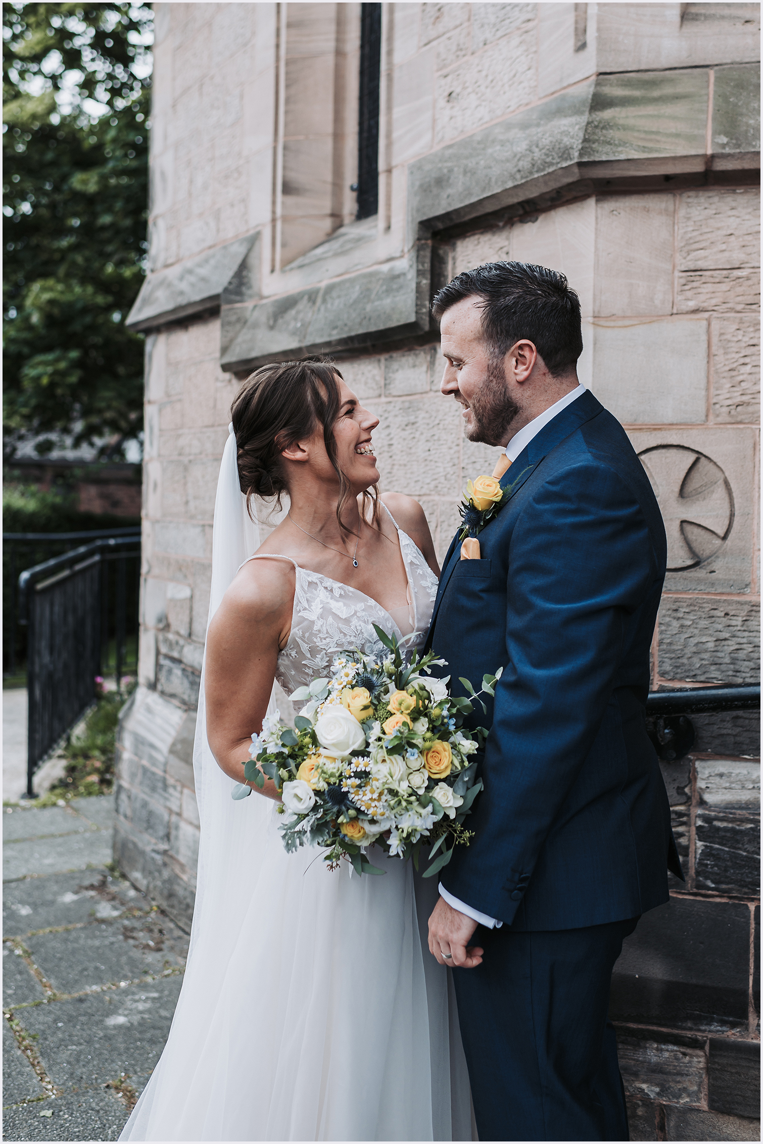 A bride and groom smile at each other outside the church where they have just got married in Chester.  Image captured by north Wales wedding photographer Helena Jayne Photography
