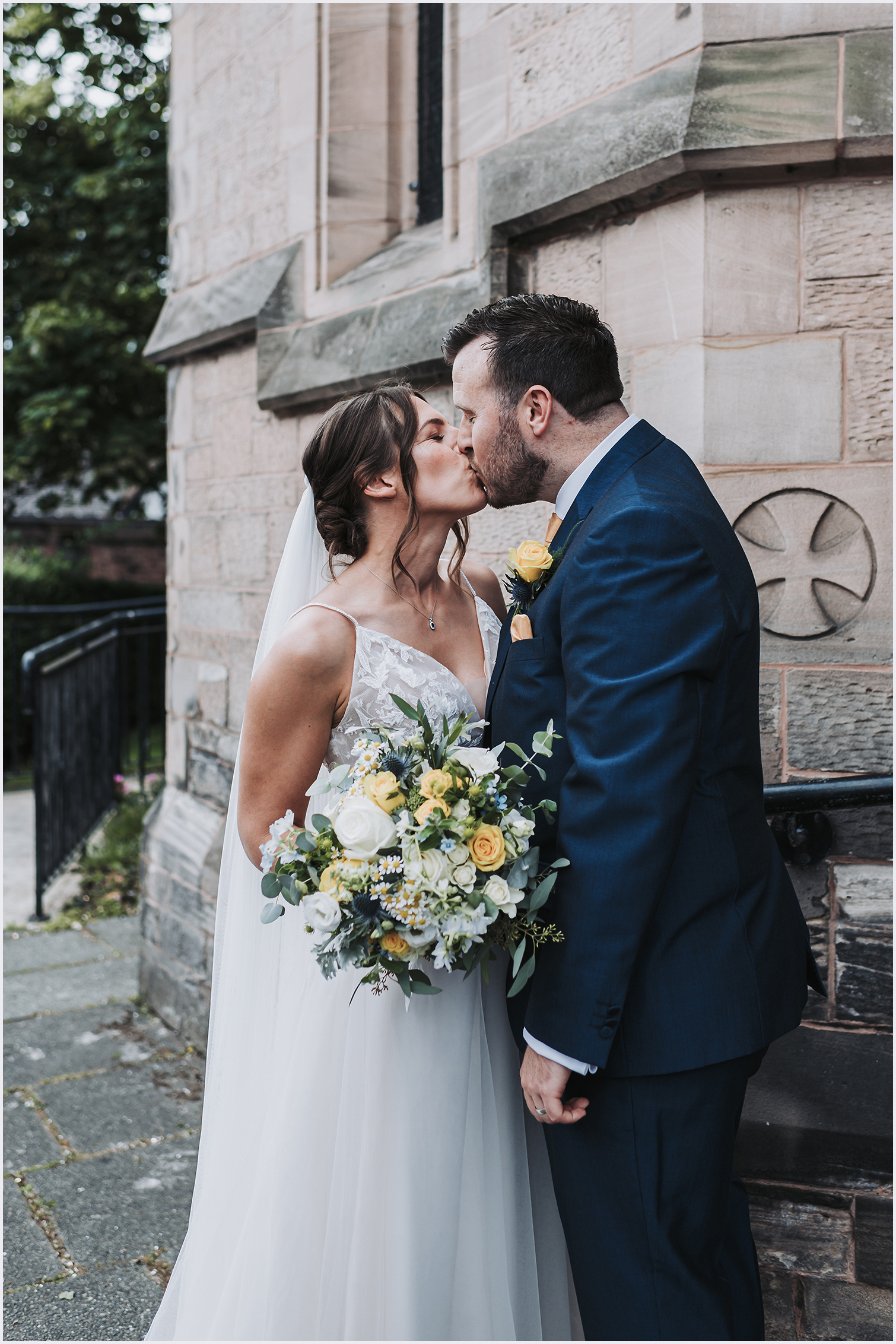 A bride and groom share a kiss  outside the church where they have just got married in Chester.  Image captured by north Wales wedding photographer Helena Jayne Photography