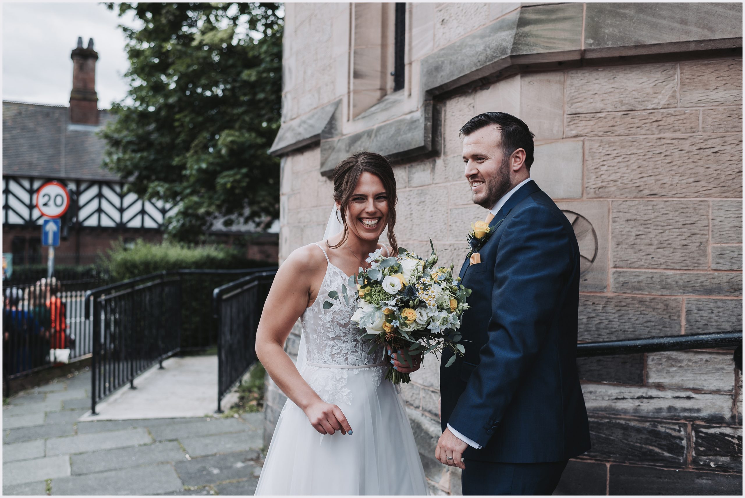 A bride and groom smile and joke outside the church where they have just got married in Chester.  Image captured by north Wales wedding photographer Helena Jayne Photography