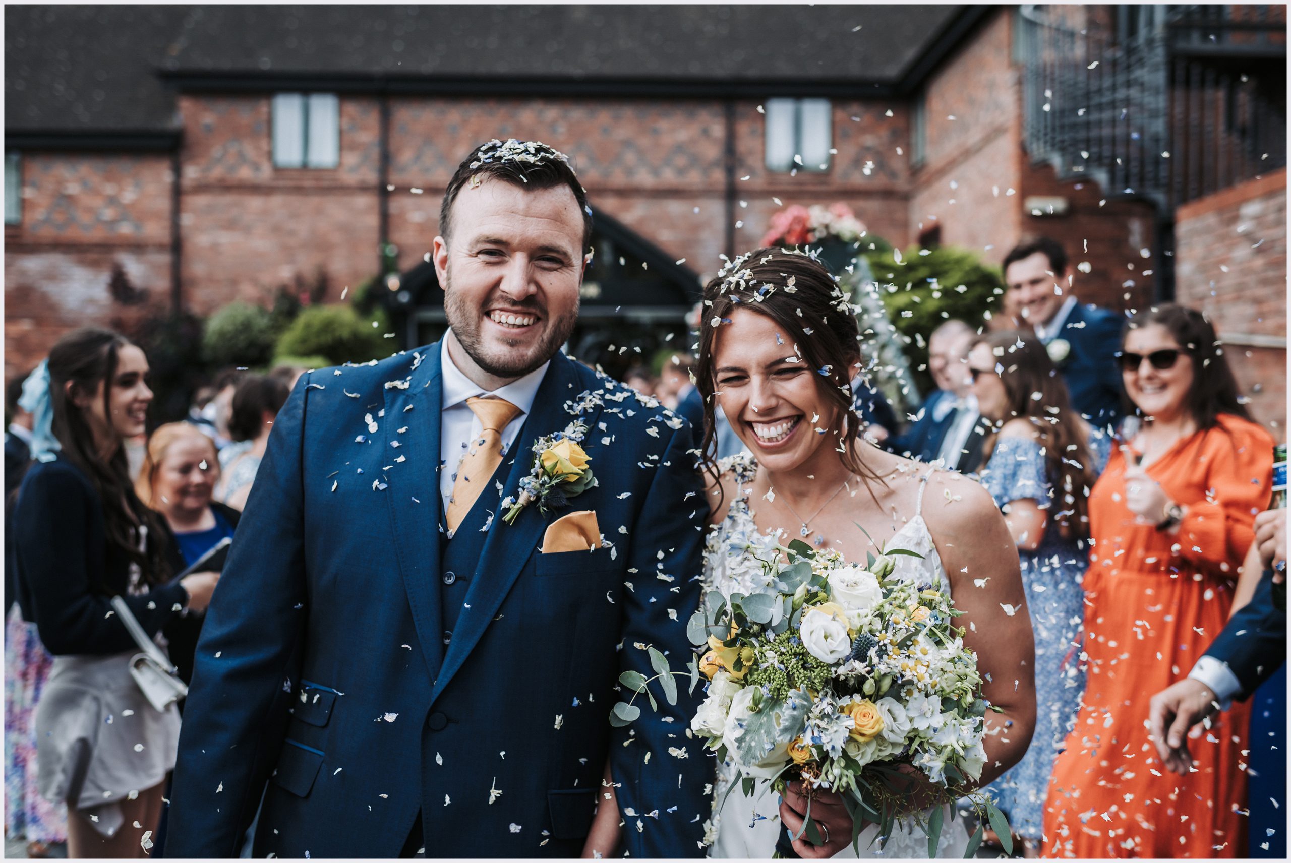 Guests shower a beeming smiling couple with confetti at The Grosvenor Pulford Hotel and Spa.  Image captured by wedding photographer Helena Jayne Photography, a wedding photographer based in north Wales