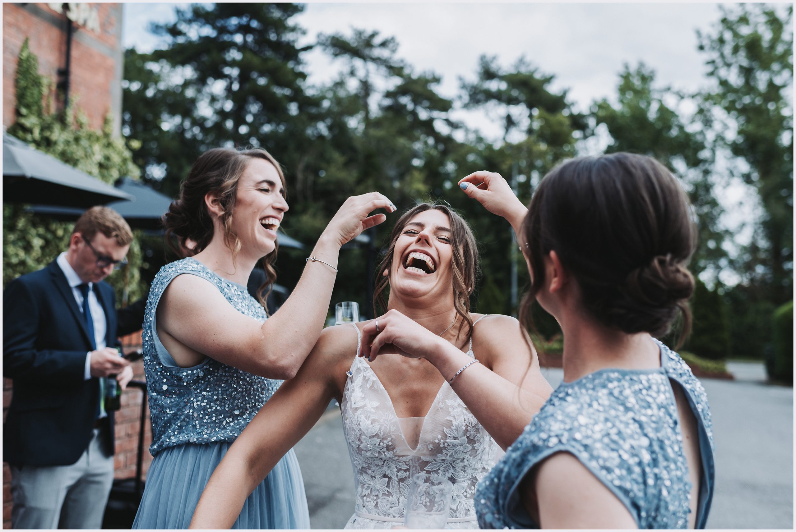 A bride with her head thrown back laughs as her bridesmaids remove confetti from her hair.  Image captured by Grosvenor Pulford Hotel and Spa wedding photographer Helena Jayne Photography
