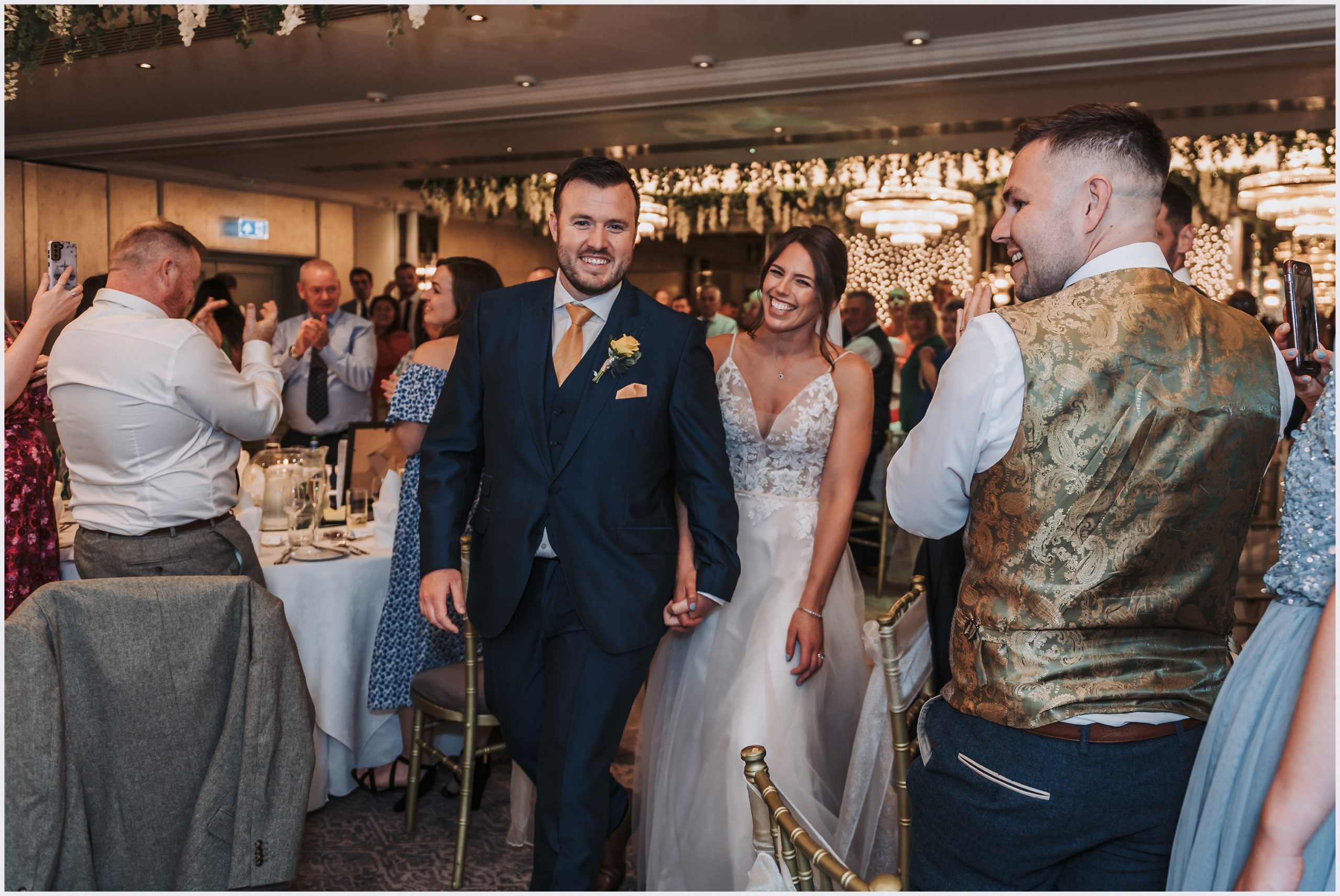 The bride and groom enter the wedding breakfast room while their guests stand and applaud their entrance.  Image captured by Helena Jayne Photography a wedding photographer based in north Wales