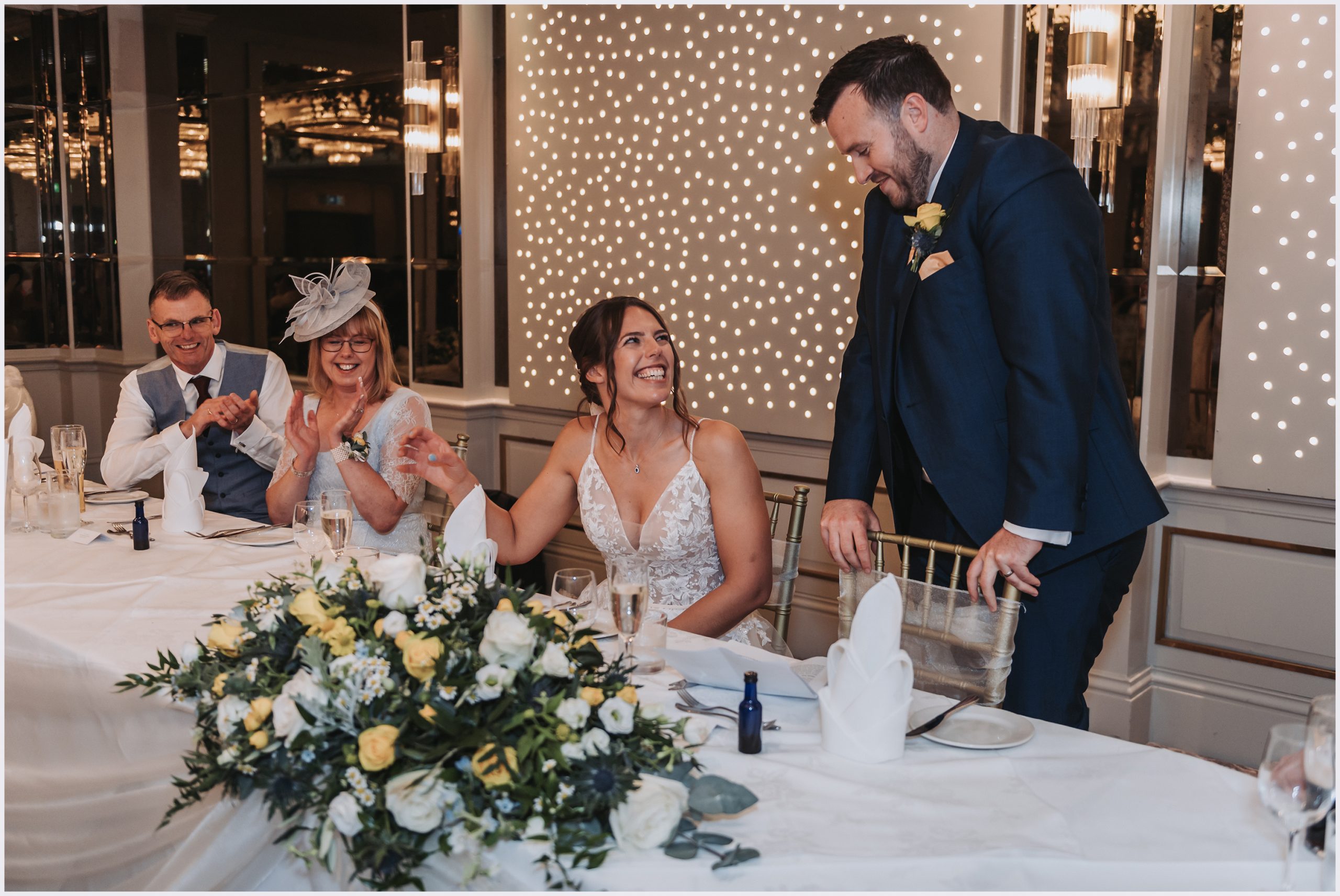 A bride looks up at her husband smiling while he makes his speech at their wedding at The Grosvenor Pulford Hotel and Spa