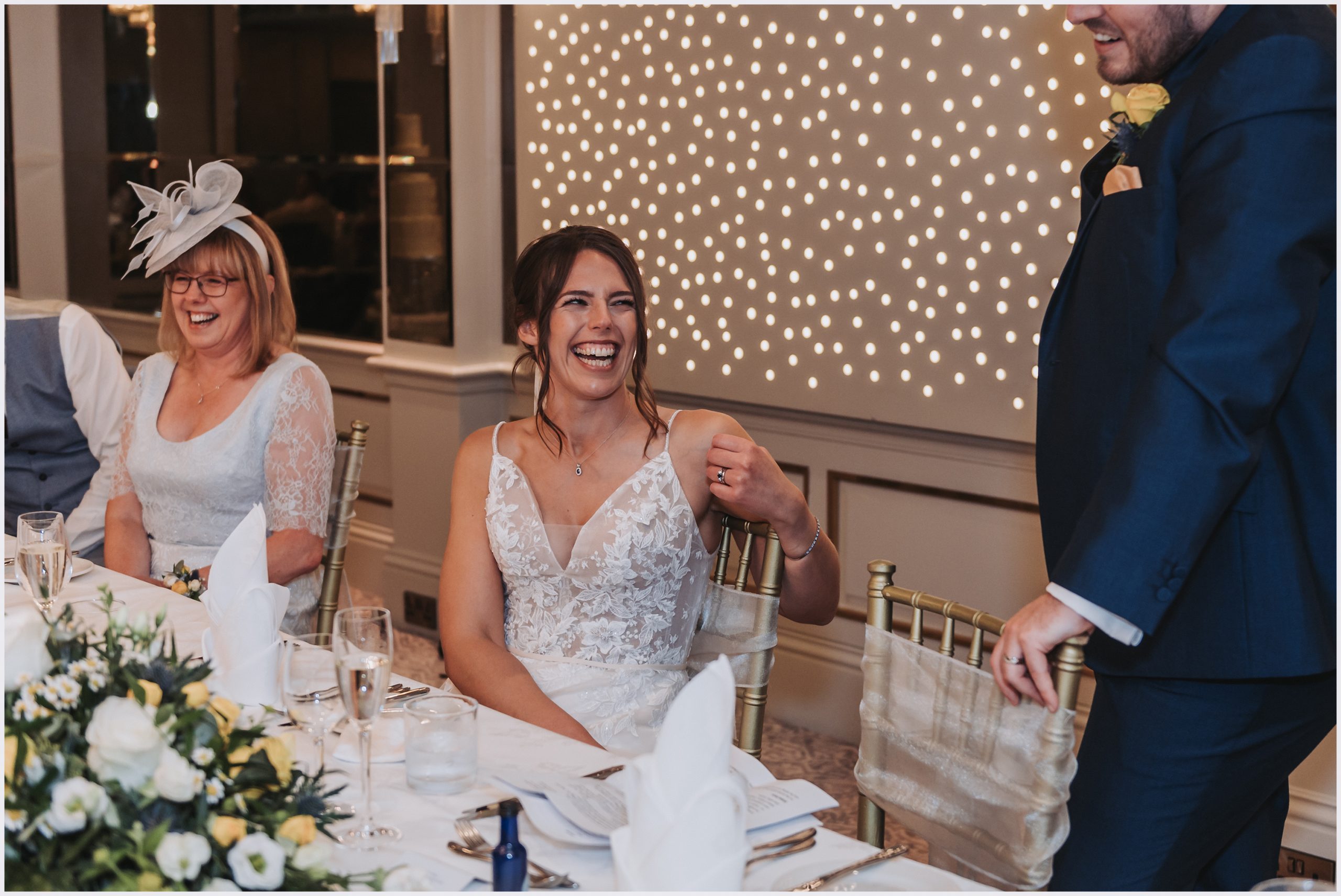 A bride looks up at her husband smiling while he makes his speech at their wedding at The Grosvenor Pulford Hotel and Spa.  Image captured by Helena Jayne Photography a north Wales based wedding photographer