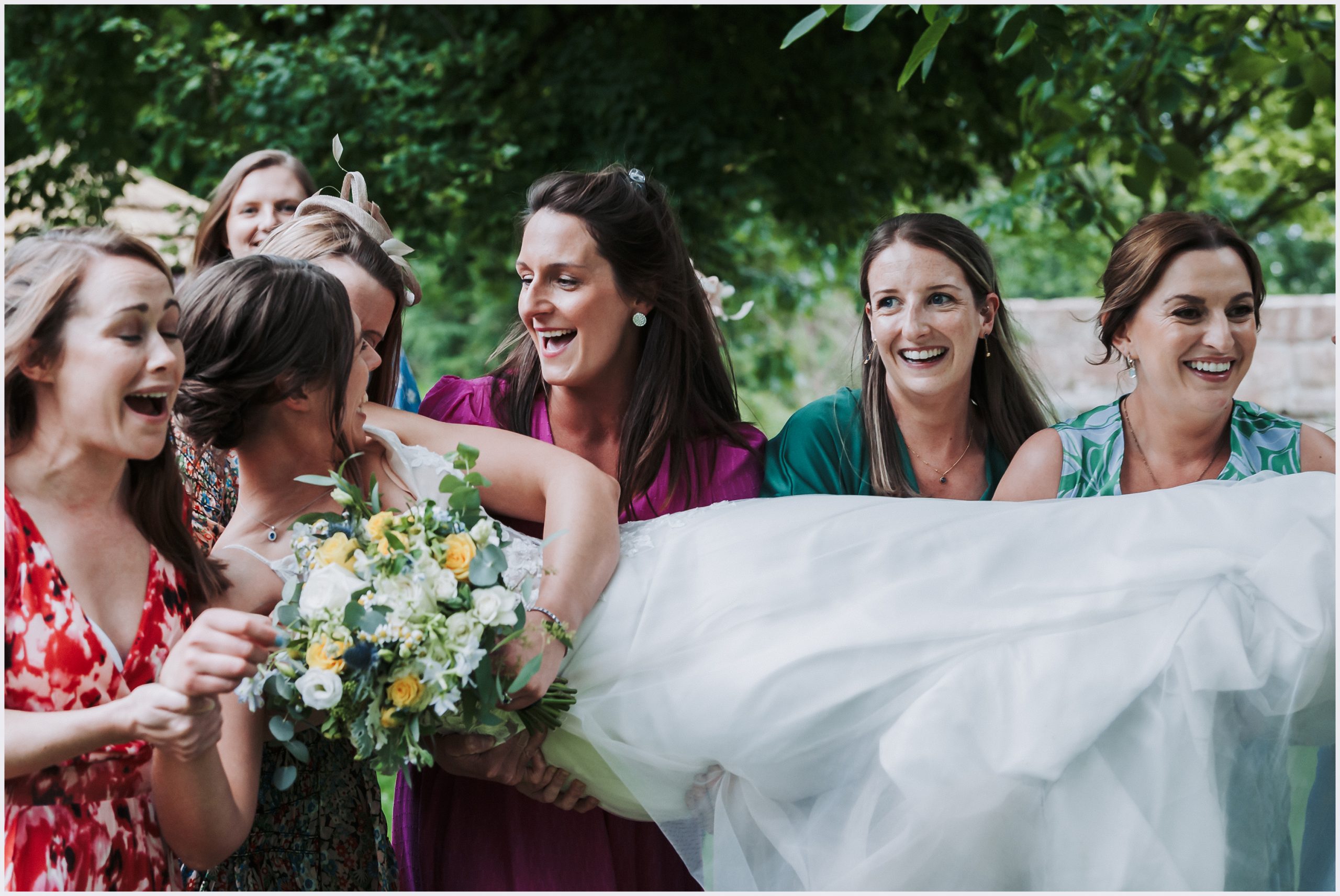 A bride laughs hysterically as she is carried by her friends during her wedding reception in the gorgeous grounds of The Grosvenor Pulford Hotel and Spa.  Image captured by Grosvenor Pulford wedding photographer Helena Jayne Photography