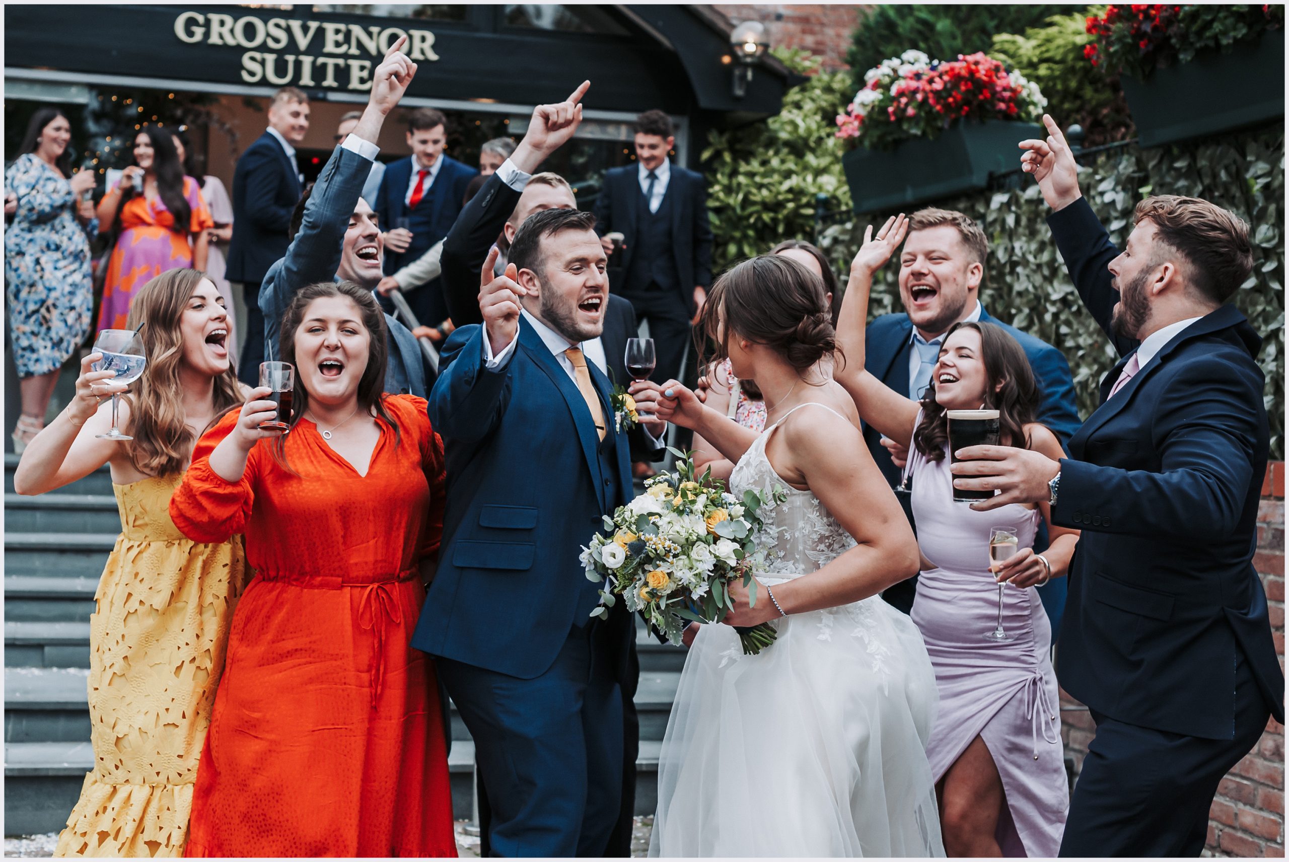 A group of friends laugh and joke with the bride and groom outside the entrance of the Grosvenor Pulford Hotel and Spa. Image captured by Grosvenor Pulford wedding photographer Helena Jayne Photography