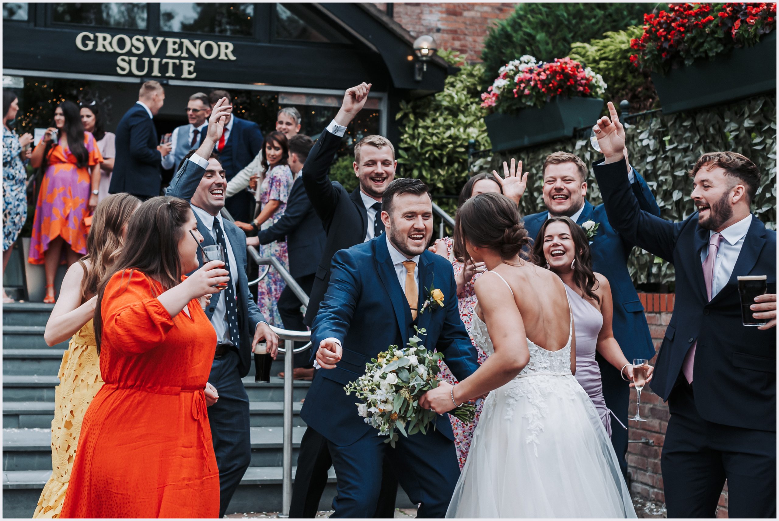 A group of friends laugh and joke with the bride and groom outside the entrance of the Grosvenor Pulford Hotel and Spa. Image captured by Grosvenor Pulford wedding photographer Helena Jayne Photography