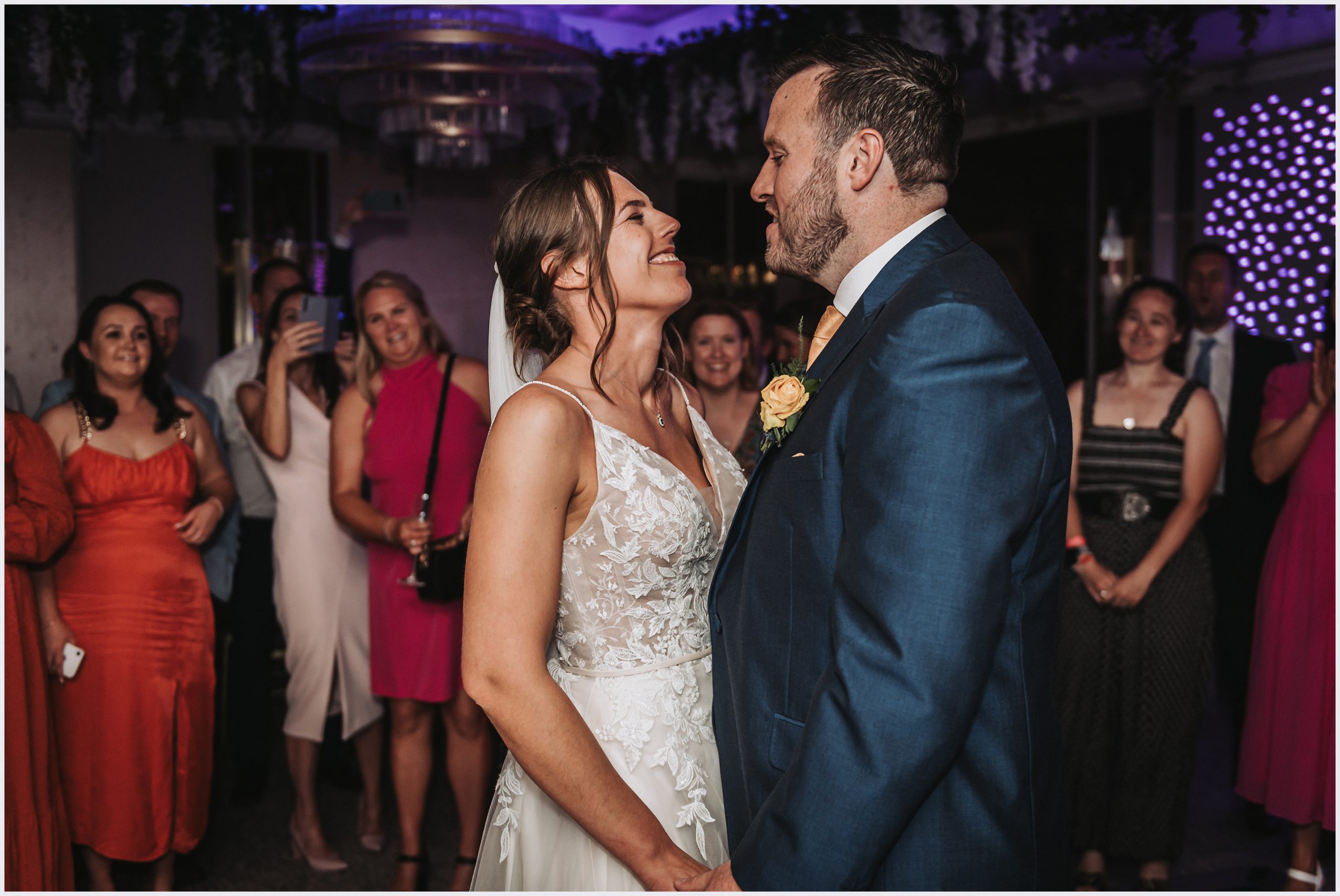 A bride and groom stare into each other's eyes during their first dance as their friends and family smile and take photographs.  Image taken by Helena Jayne Photography a preferred supplier of The Grosvenor Pulford Hotel and Spa