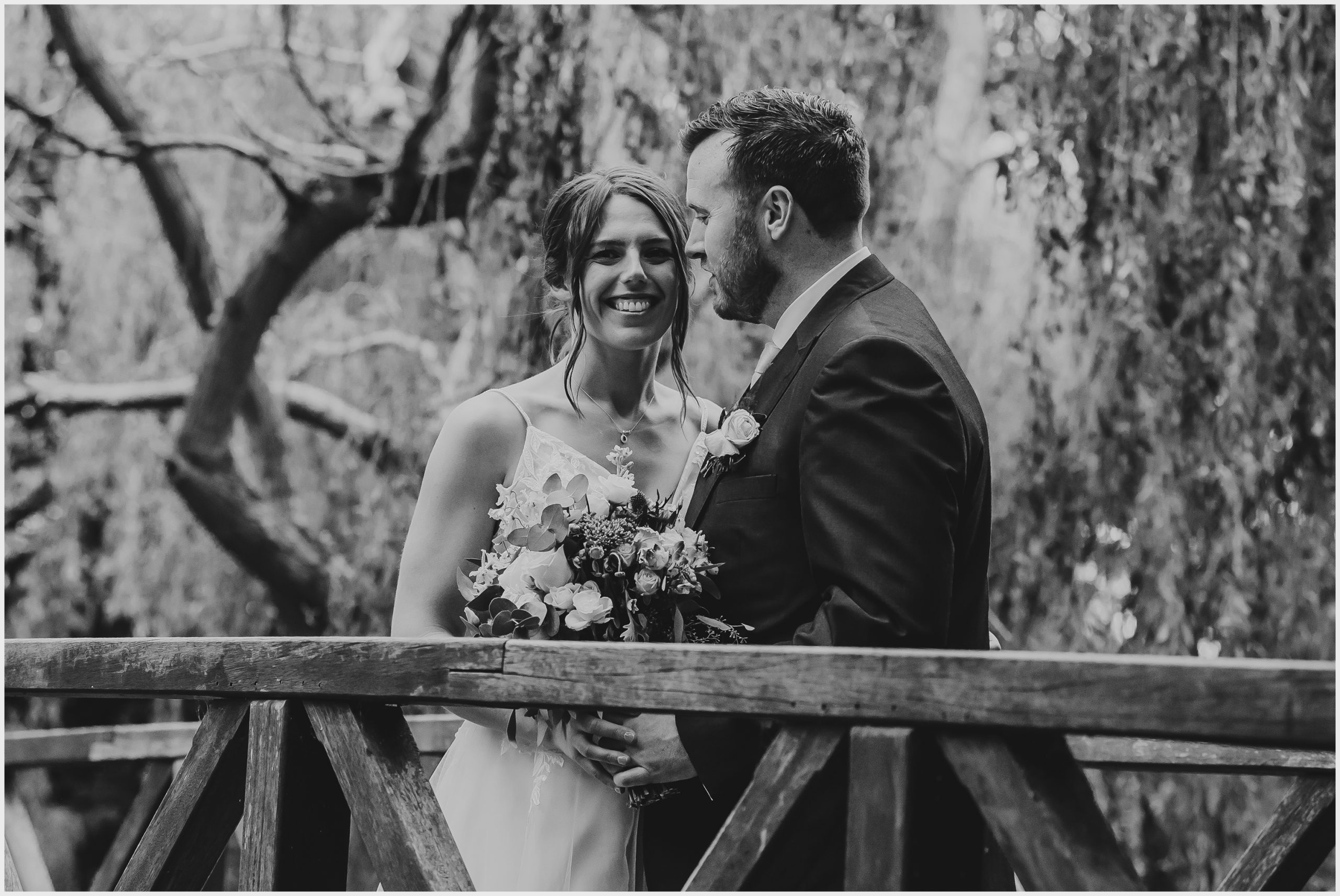 A beaming bride looks at the camera while being hugged by her husband during their couples photoshoot at The Grosvenor Pulford Hotel and Spa.  Image captured by Helena Jayne Photography a wedding photographer based in Chester