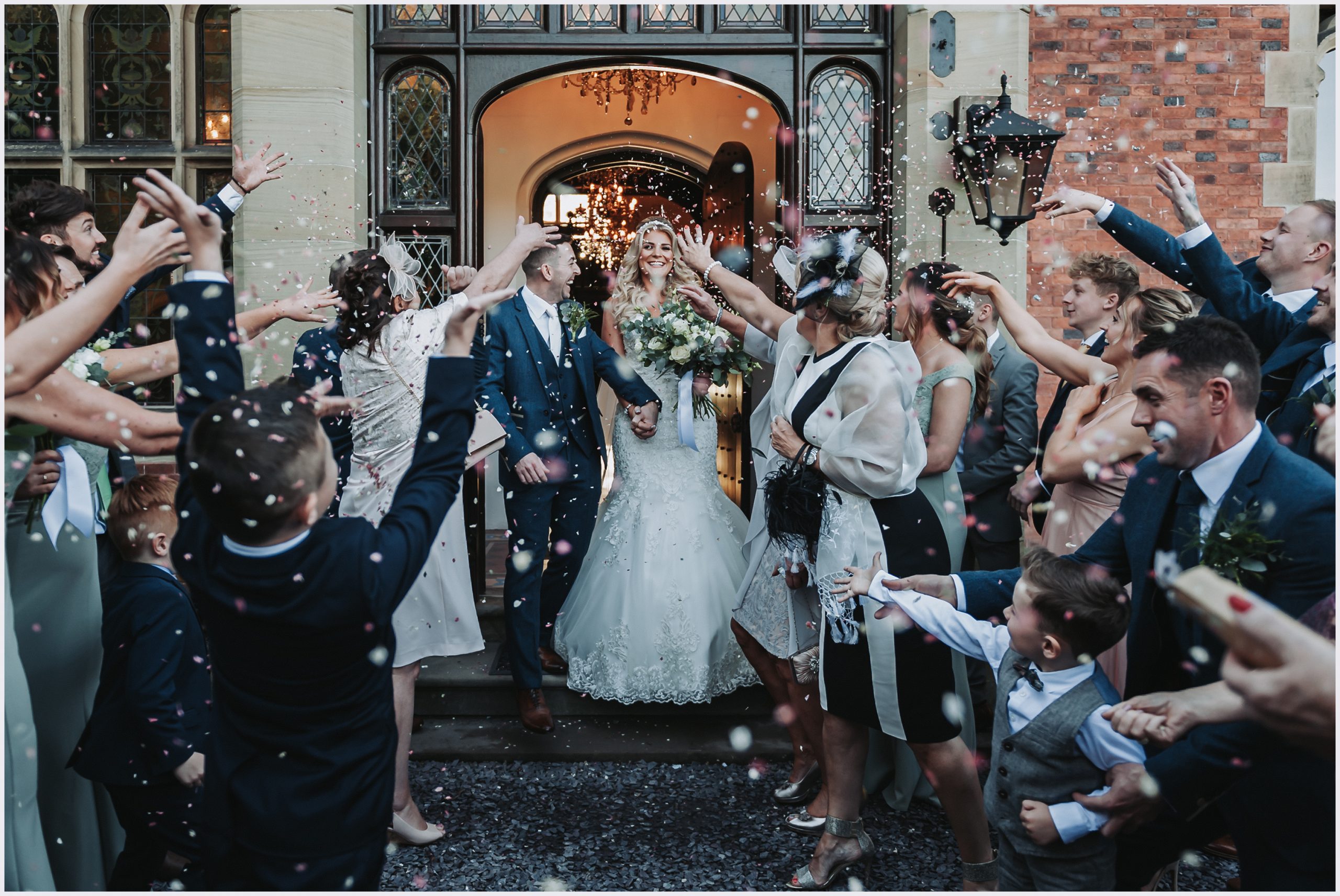 A beaming, smiling brides looks at all her guests as she walks out of the front door of Tyn Dwr Hall.  The are showering her and her new husband with confetti.  Image captured by North Wlaes wedding photographer Helena Jayne Photography