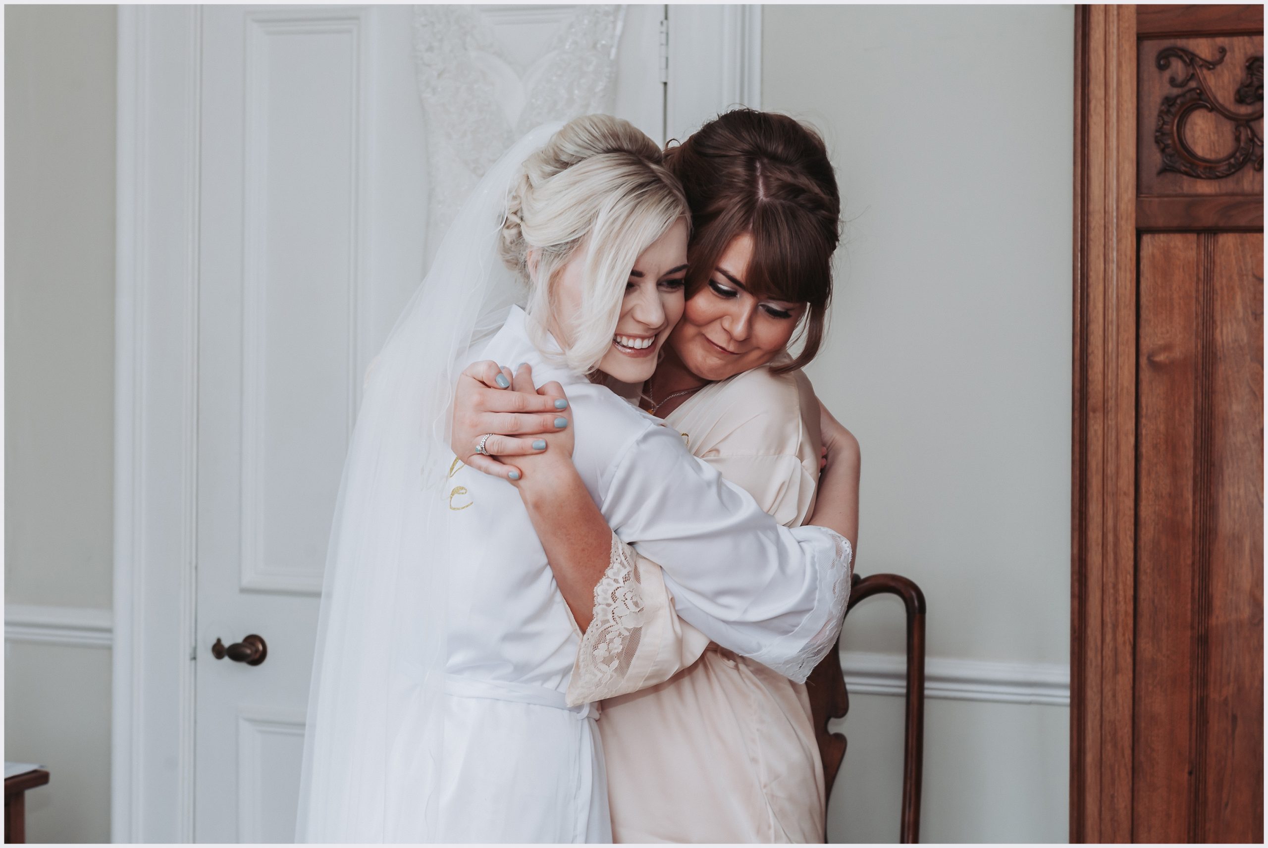 A bride and her bridesmaid embrace smiling on the morning of the wedding.  Image captured by Helena Jayne Photography by north Wales based photographer Helena Jayne Photography