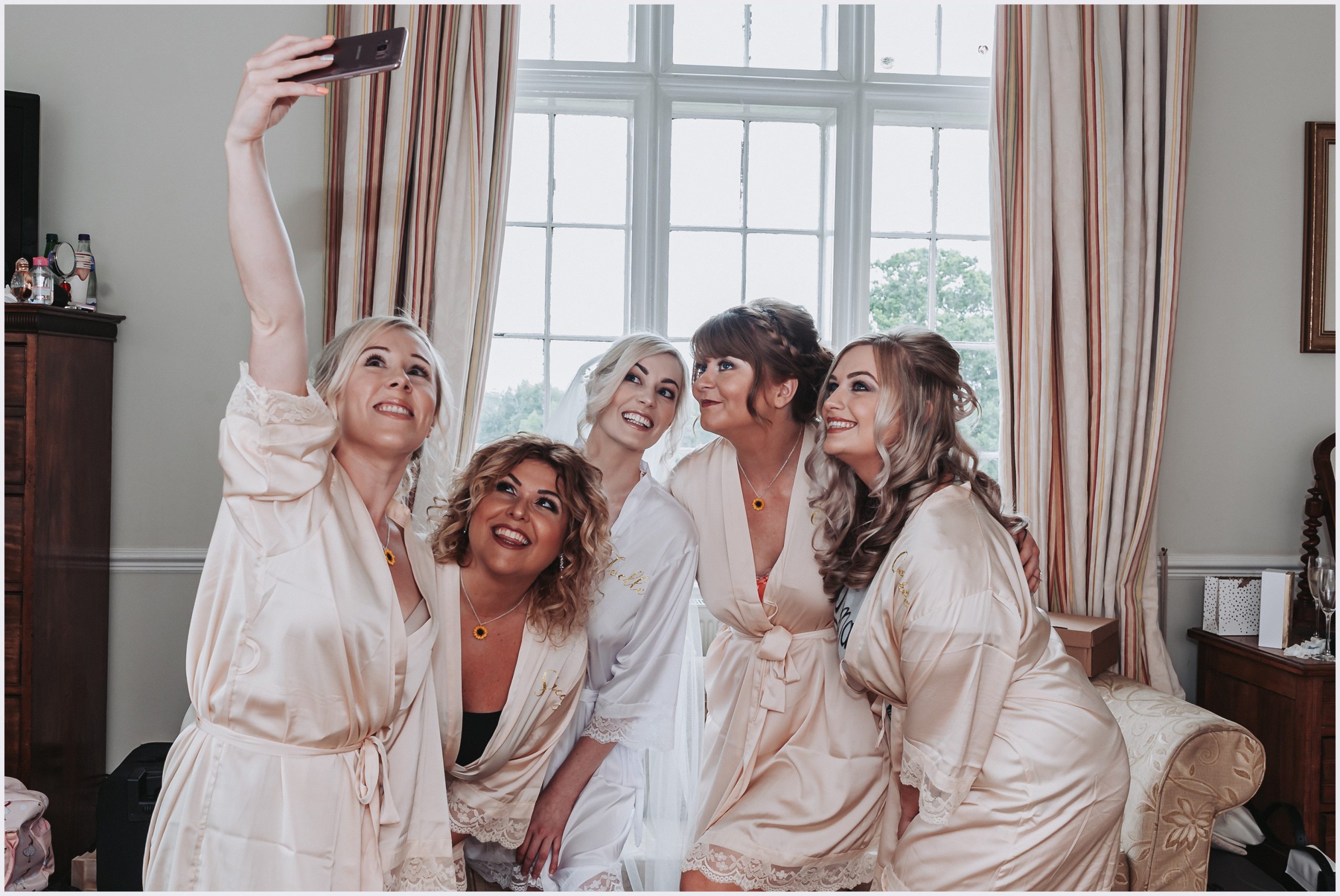 A beautiful bride and her bridesmaids wearing matching dressing gowns pose together for a selfie during the morning preparations.  Image captured at Willington Hall Hotel by Helena Jayne Photography a north Wales based photographer