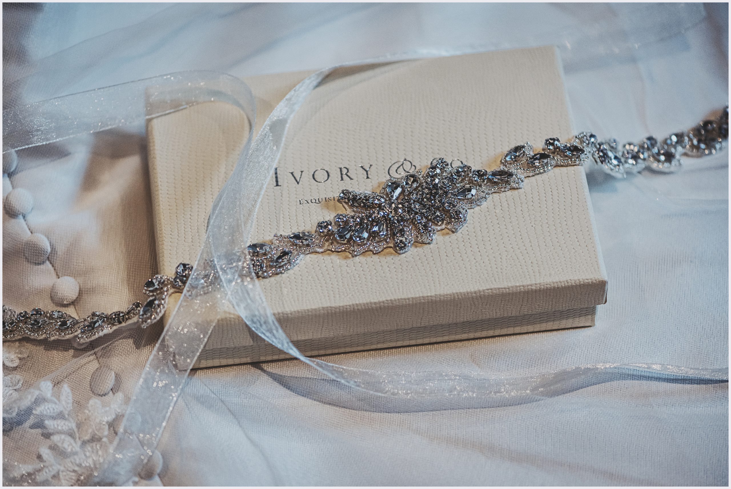 A bride's diamanté wedding dress belt rests on the box surrounded by ribbon.