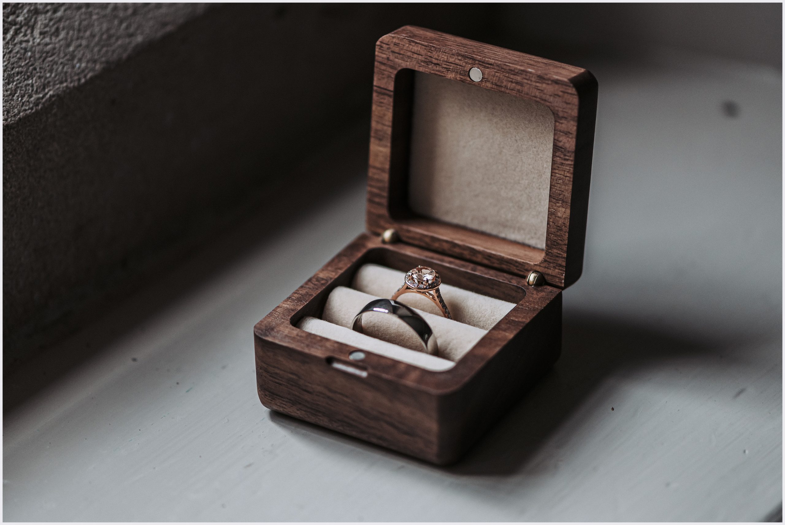 An open beautiful wooden ring box open displaying a bride and groom's wedding rings.