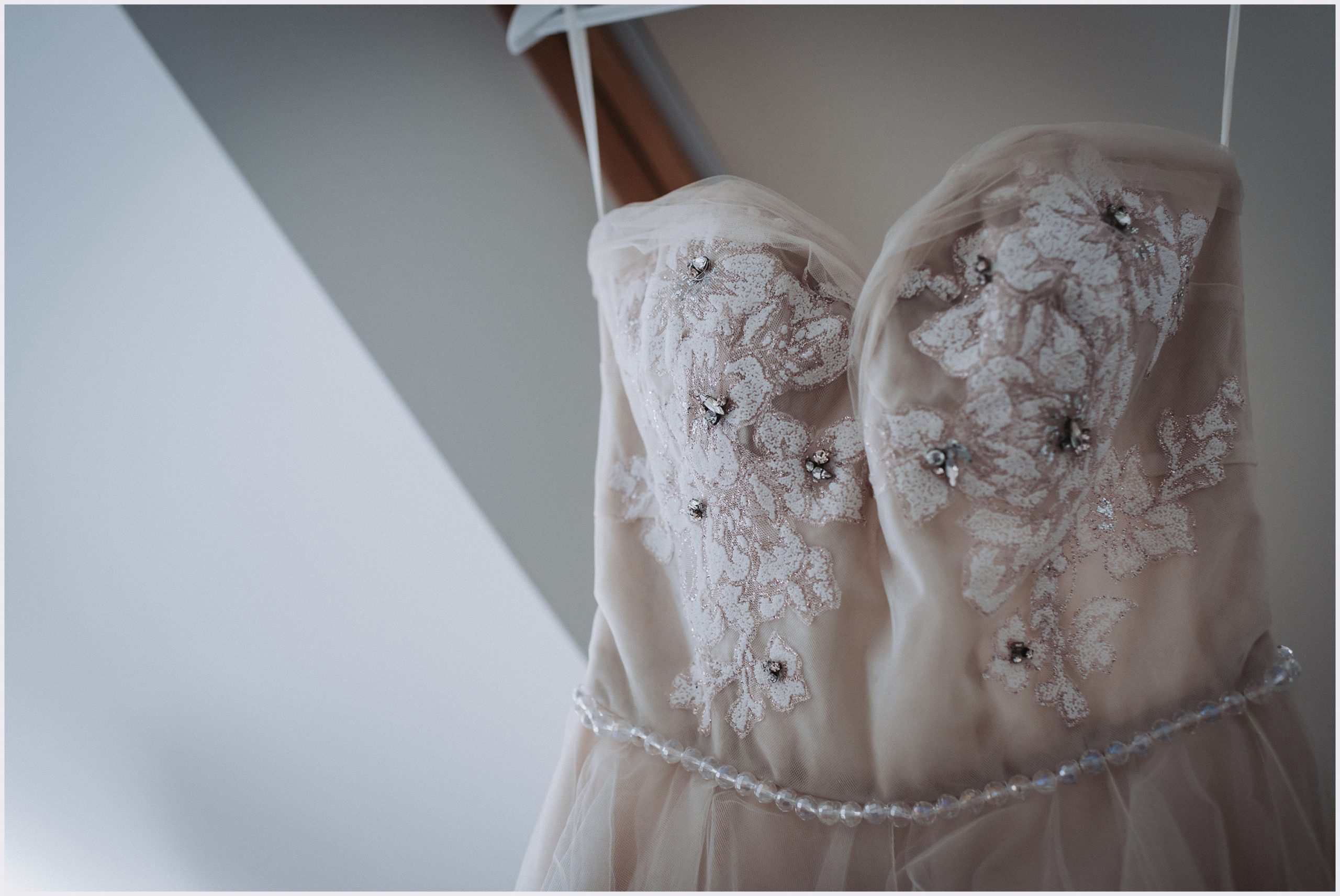 The bodice of a bride's beautiful wedding dress hanging up in the wondow of a bride's dressing room.  Image captured by Cheshire wedding photographer Helena Jayne Photography