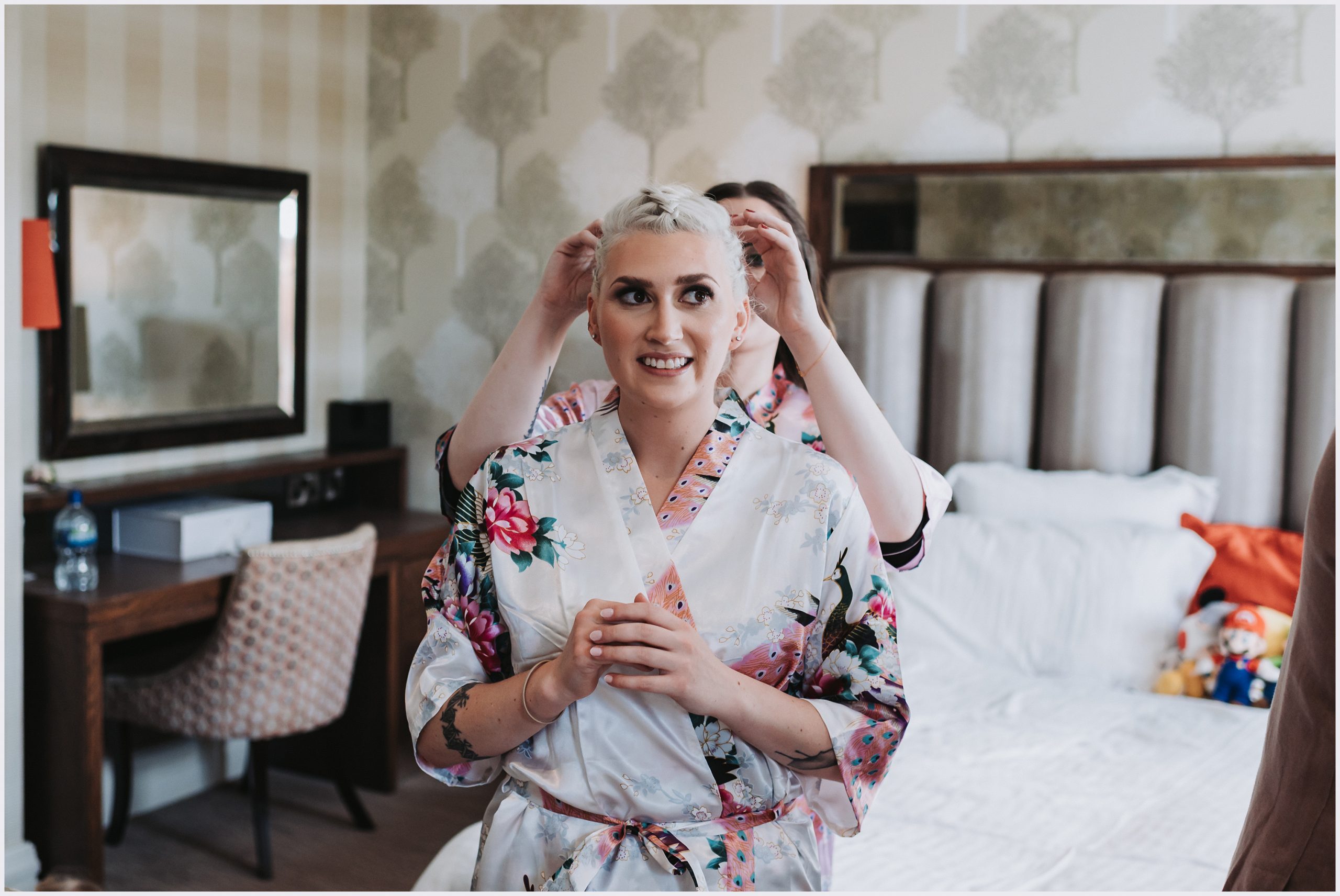 A gorgeous bride is helped by her bridesmaid to get dressed in their dressing roomm on the morning of her wedding.  Image captured by Helena Jayne Photography, a wedding photographer based in north Wales