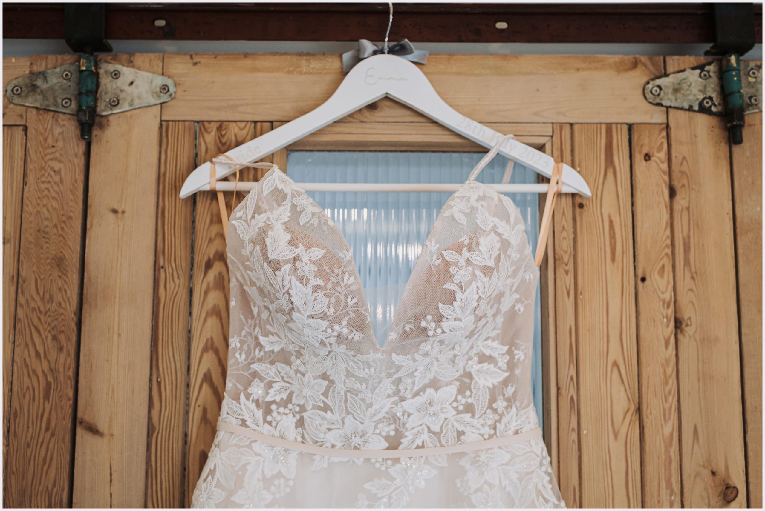 A beautiful wedding dress hanging against the rustic doors of a barn conversion
