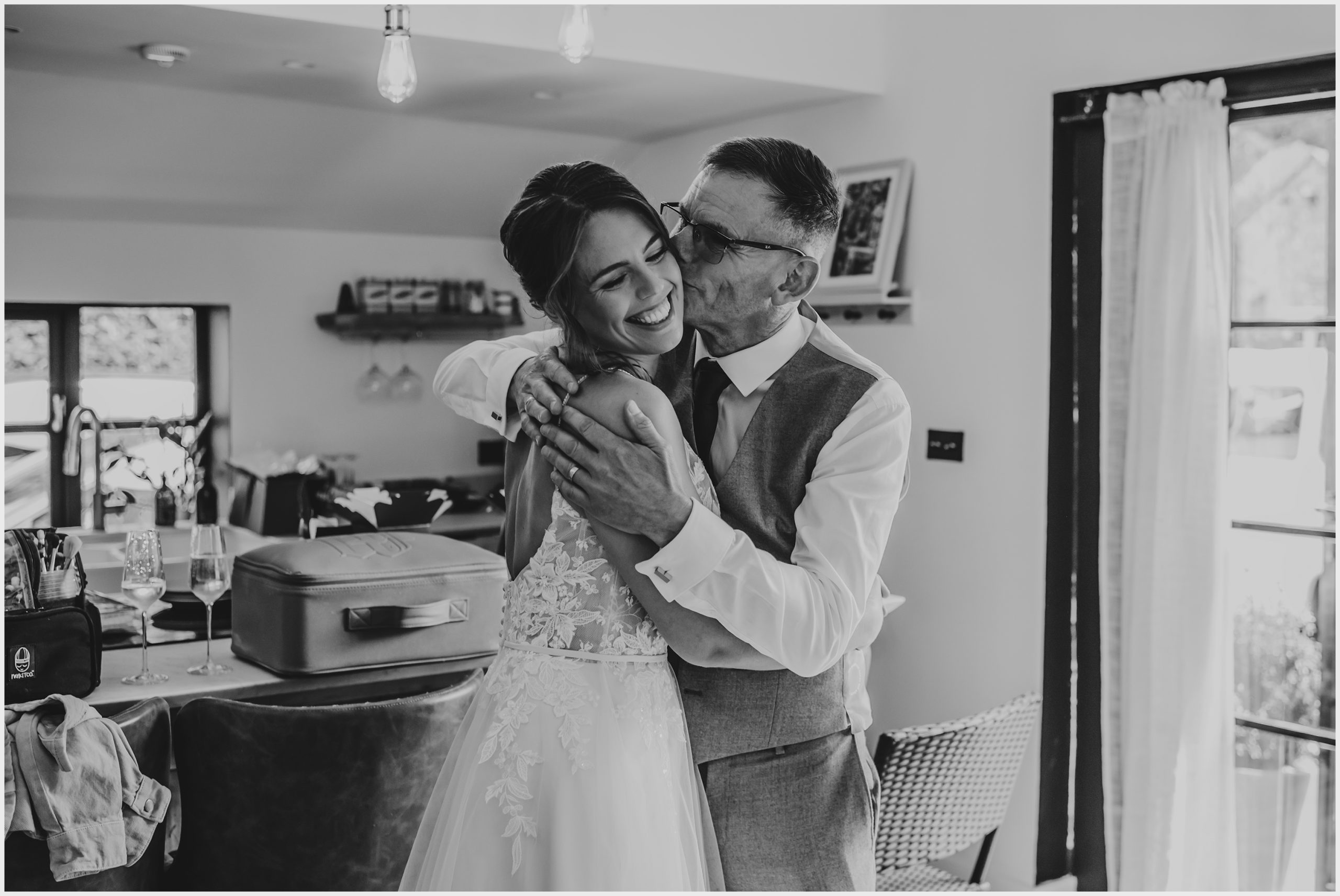 A very proud father of the bride kisses his daughter on the cheek after he has seen her for the first time.  The bride is smiling widely.  Image captured by Helena Jayne Photography a north Wales based wedding photographer