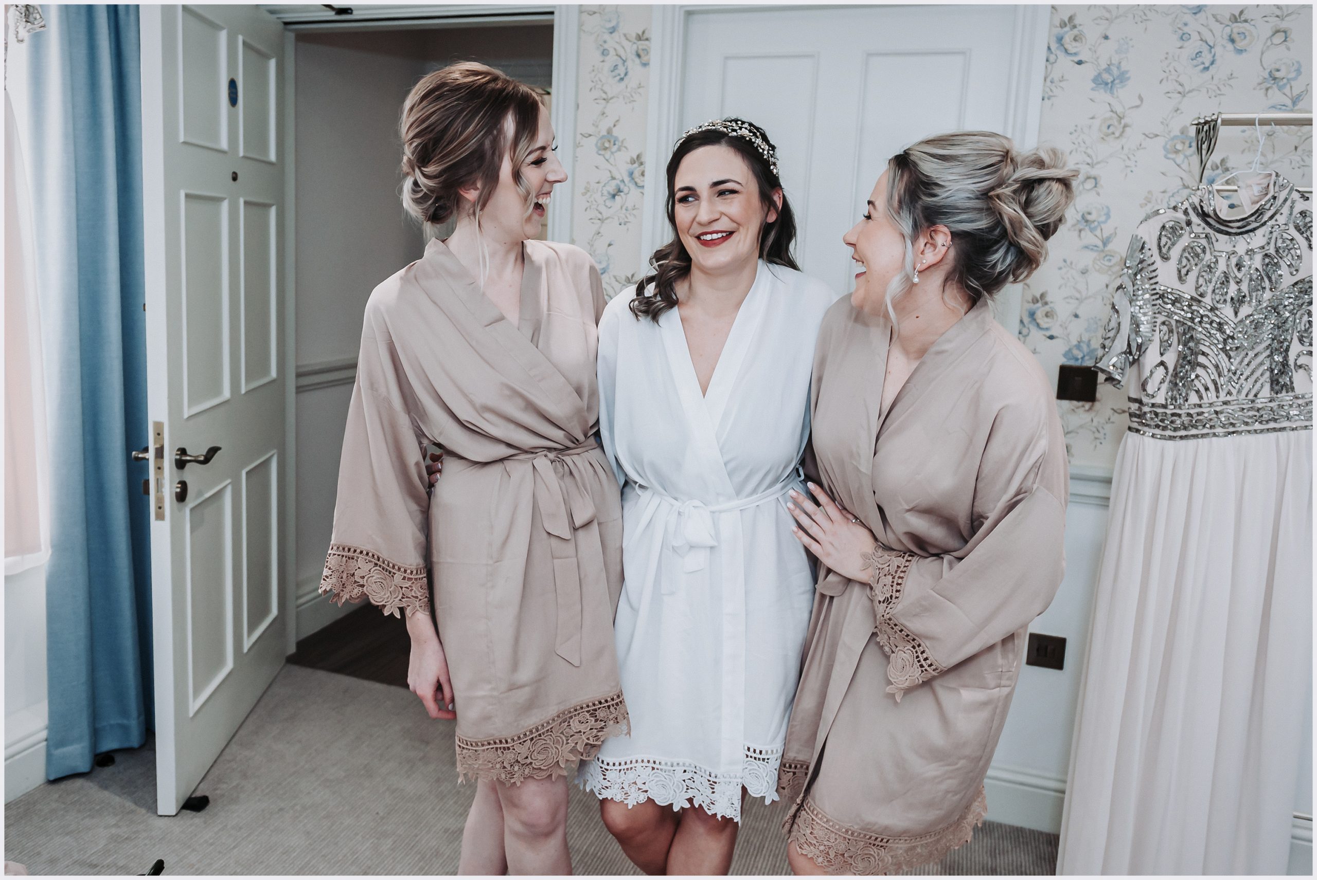 Three bridesmaids with their arms around each other share a joke in the gorgeous dressing room at Old Bishop's Palace in Chester, an exclusive wedding venue.  Image captured by Helena Jayne Photography a north Wales based photographer