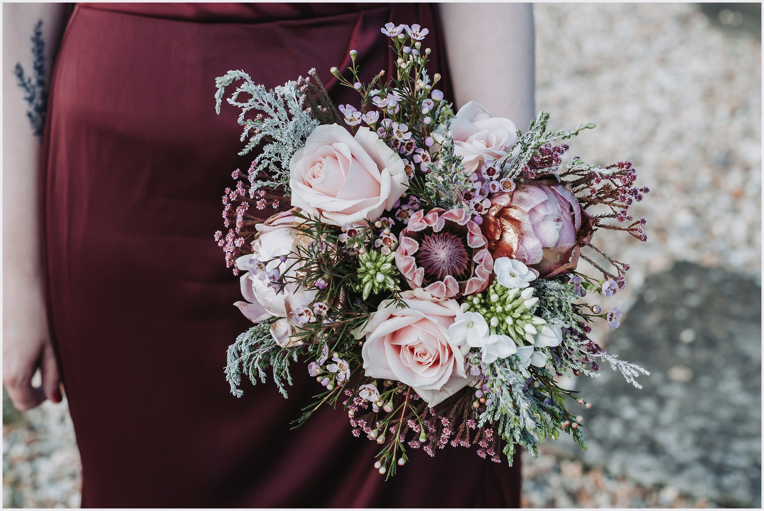 A beautiful bouquet of pastel colours and greens is held by a bridesmaid