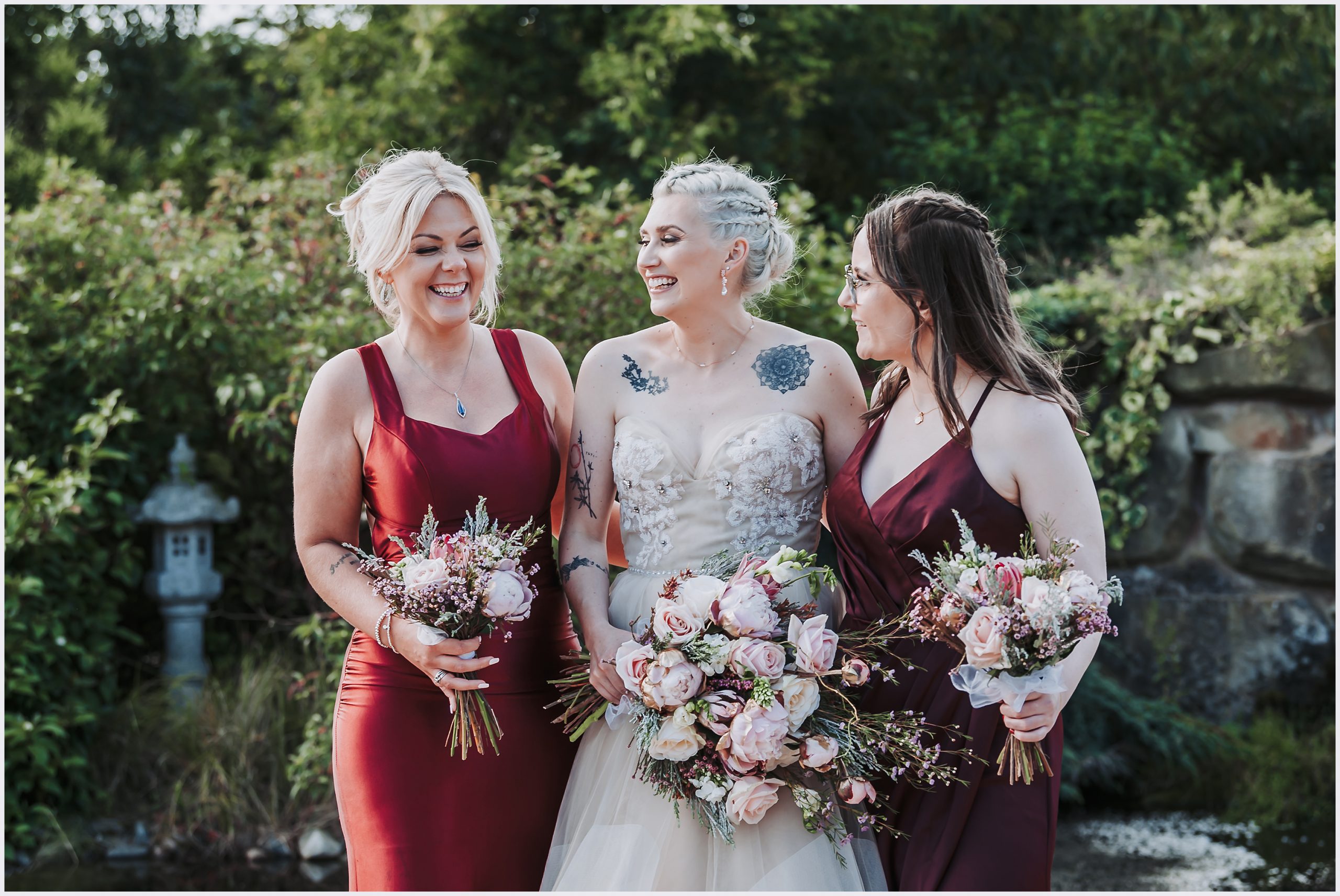A bride and her two bridesmaids share a joke together.  The three of them are laughing and joking with each other.  tehy all hold a beautiful buoquet of flowers