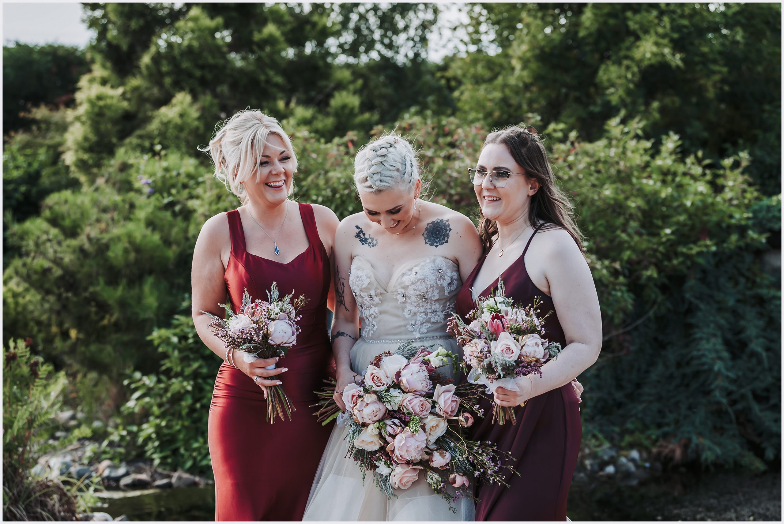 A bride and her two bridesmaids share a joke together.  The three of them are laughing and joking with each other.  They all hold a beautiful buoquet of flowers