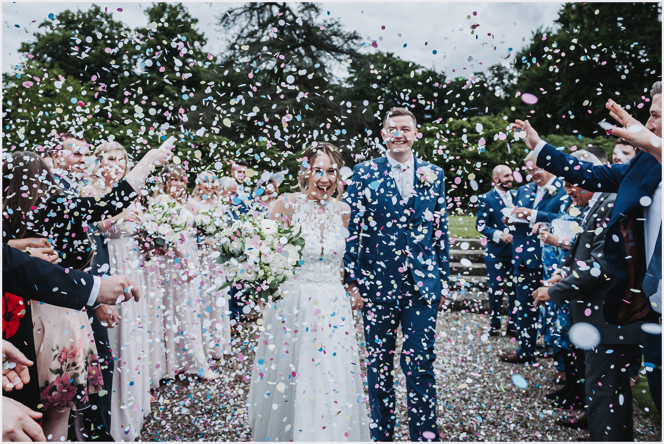 A beautiful bride and her new husband are showered in a lot of confetti after their wedding ceremony at Willington Hall Hotel.  Image captured by Cheshire Wedding Photographer Helena Jayne Photography