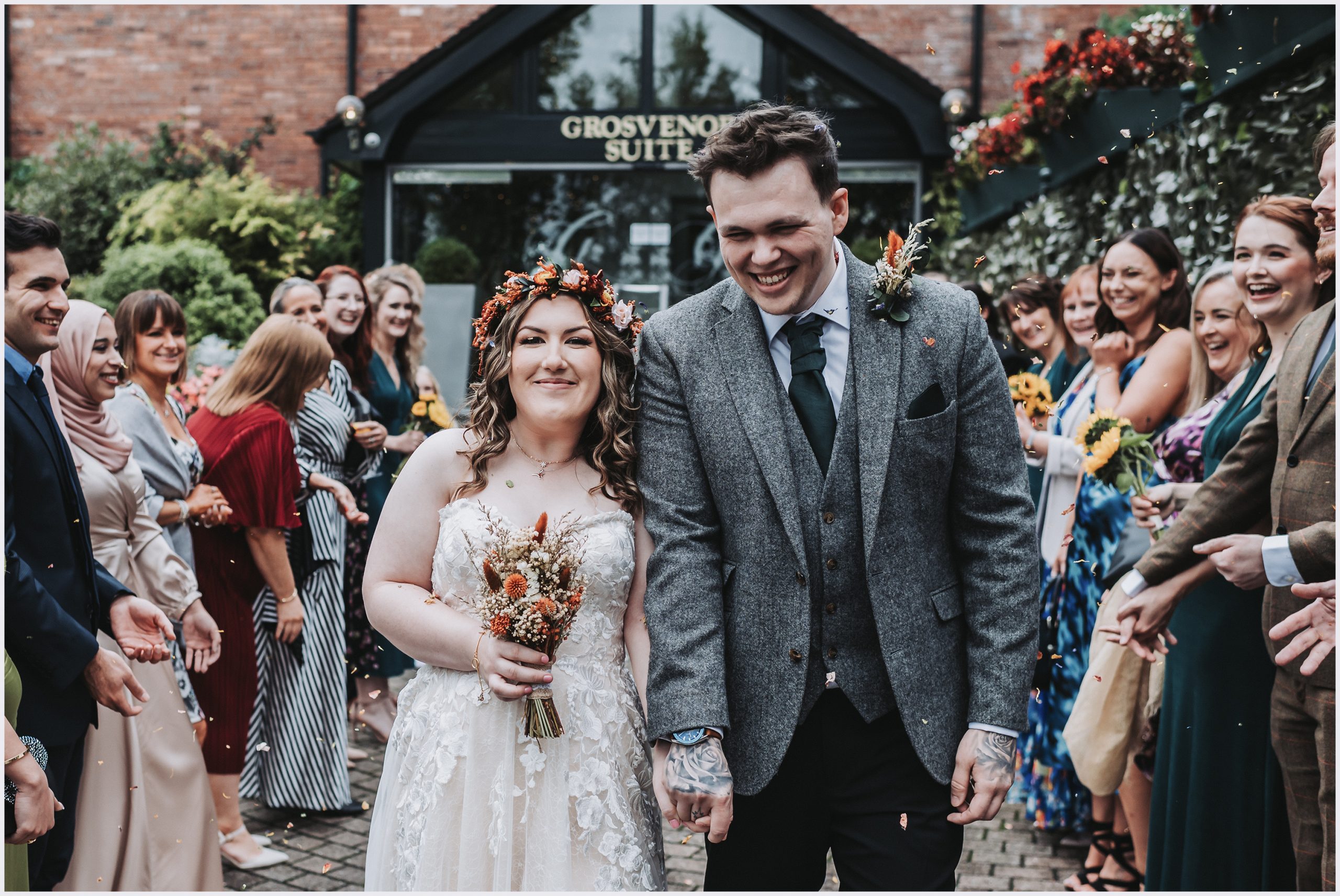 A beautiful bride and her new husband smile and laugh as guests shower them with confetti after the wedding ceremony.  Image captured by north wales wedding photographer Helena Jayne Photography
