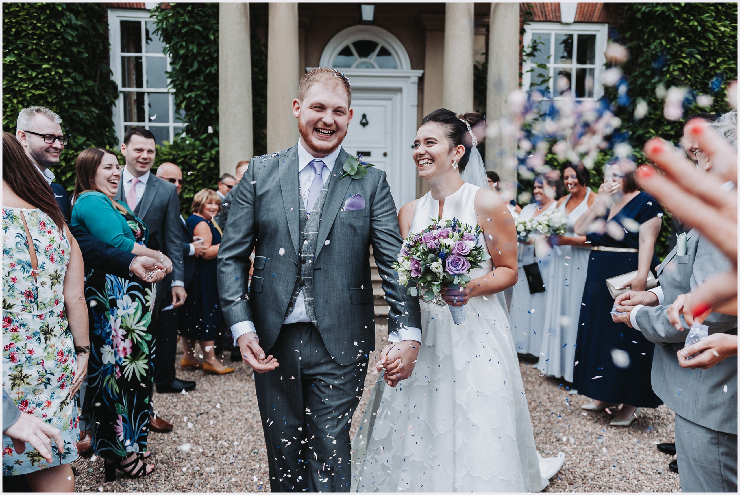 A beautiful bride smiles at her new husband as their guests shower them with confetti outside Iscoyd Park.  Image captured by Helena Jayne Photography Cheshire and north Wlaes Wedding Photographer